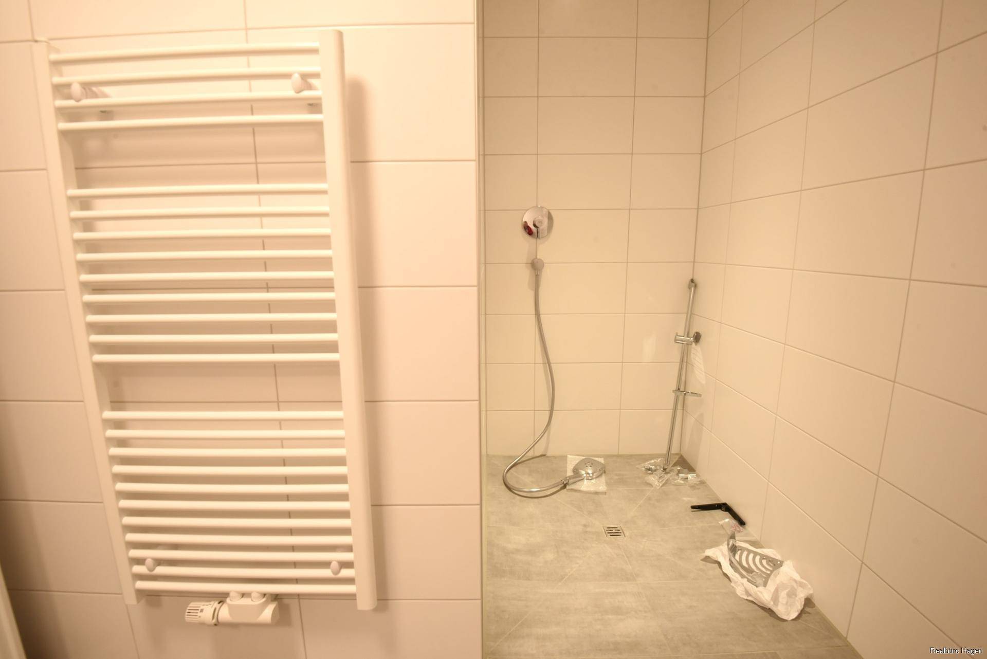 Duschbereich im Badezimmer mit weißen Fliesen und Handtuchheizkörper.