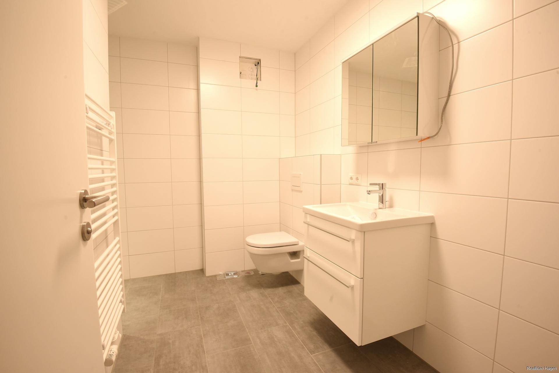 Modernes Badezimmer mit weißen Fliesen, Waschtisch und wandhängendem WC.