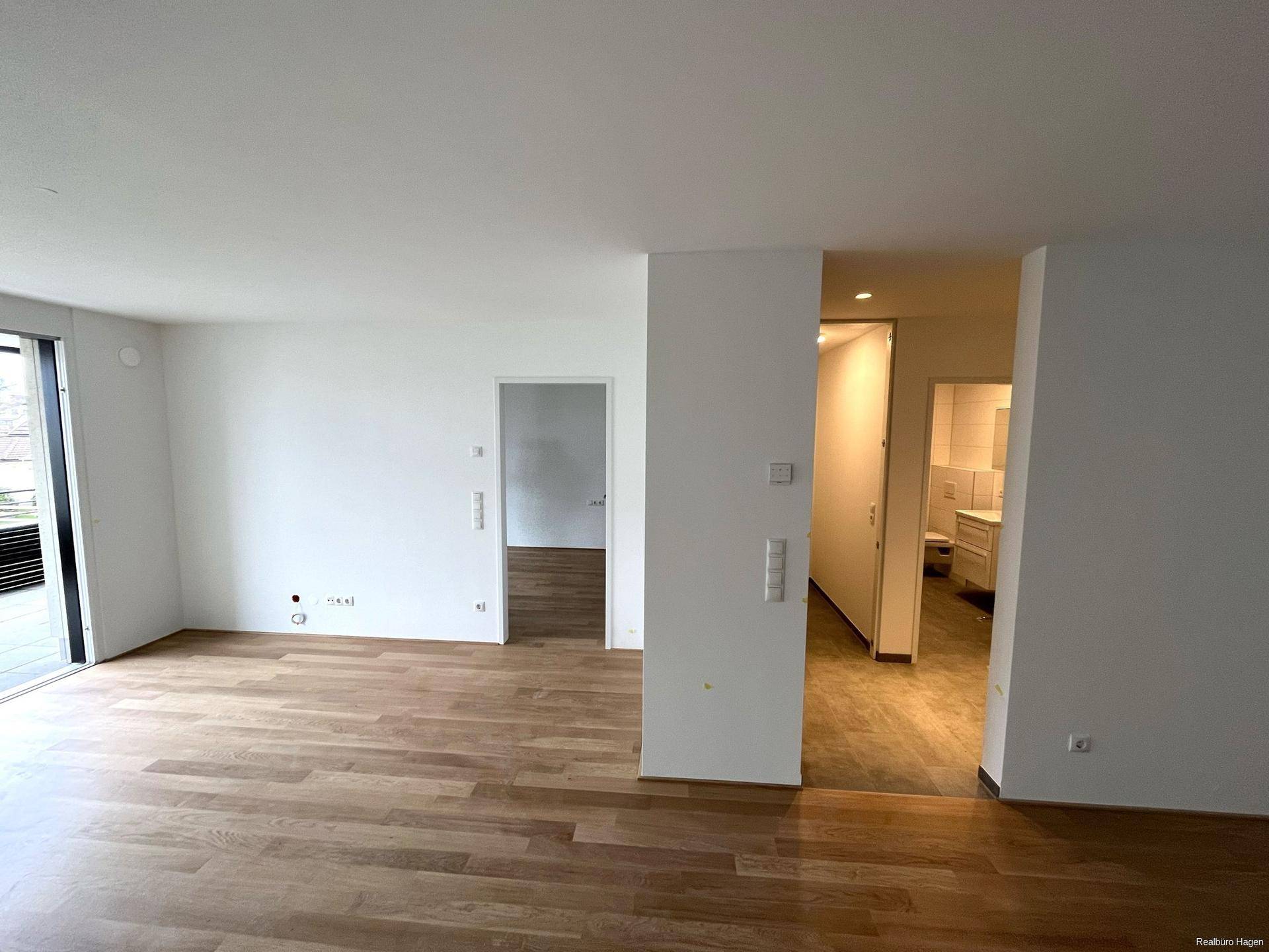 Heller Wohnbereich mit Parkettboden und Zugang zu weiteren Räumen sowie einem Balkon.