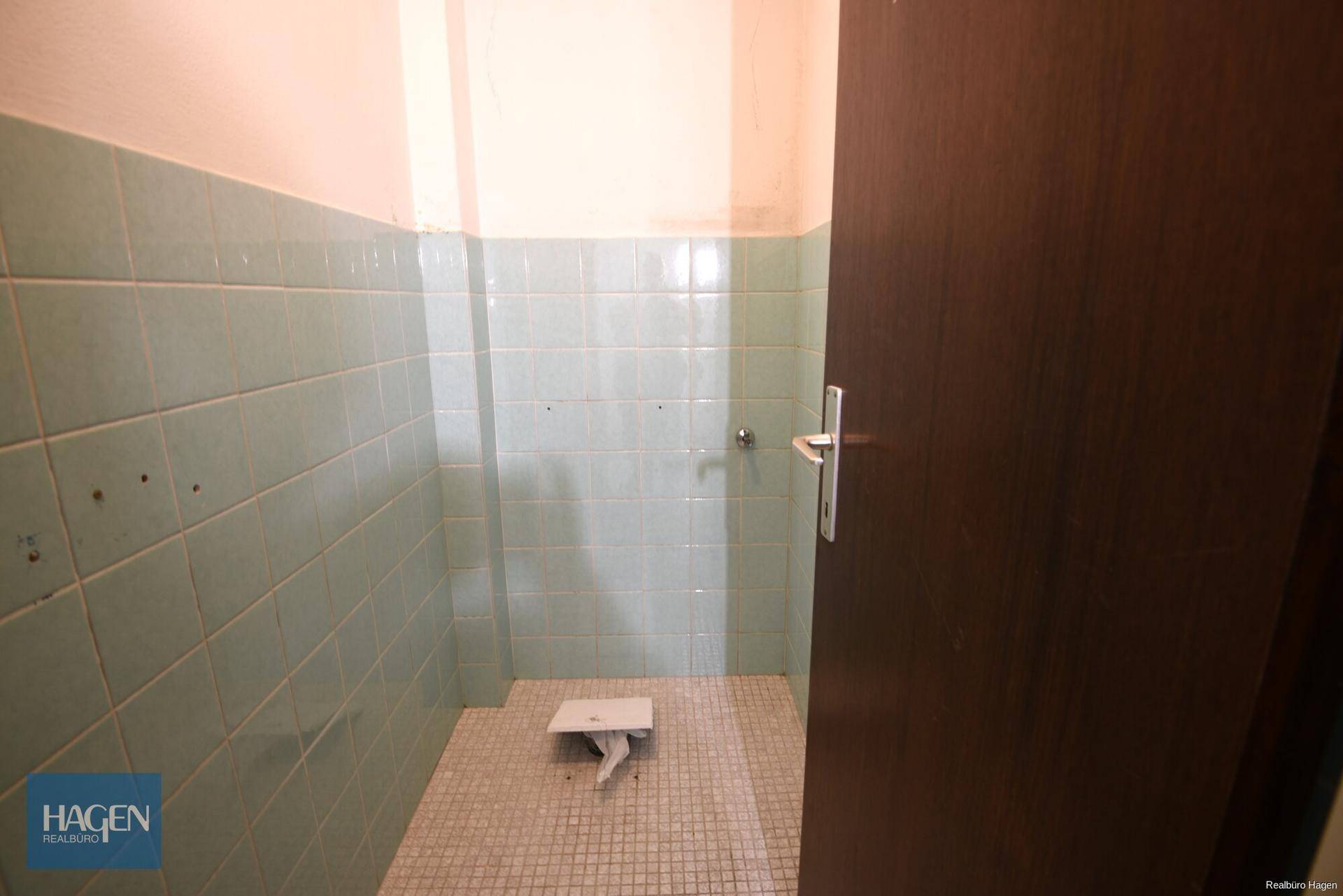 Separate Toilette mit grünen Wandfliesen und Mosaikboden, funktional und renovierungsbedürftig.