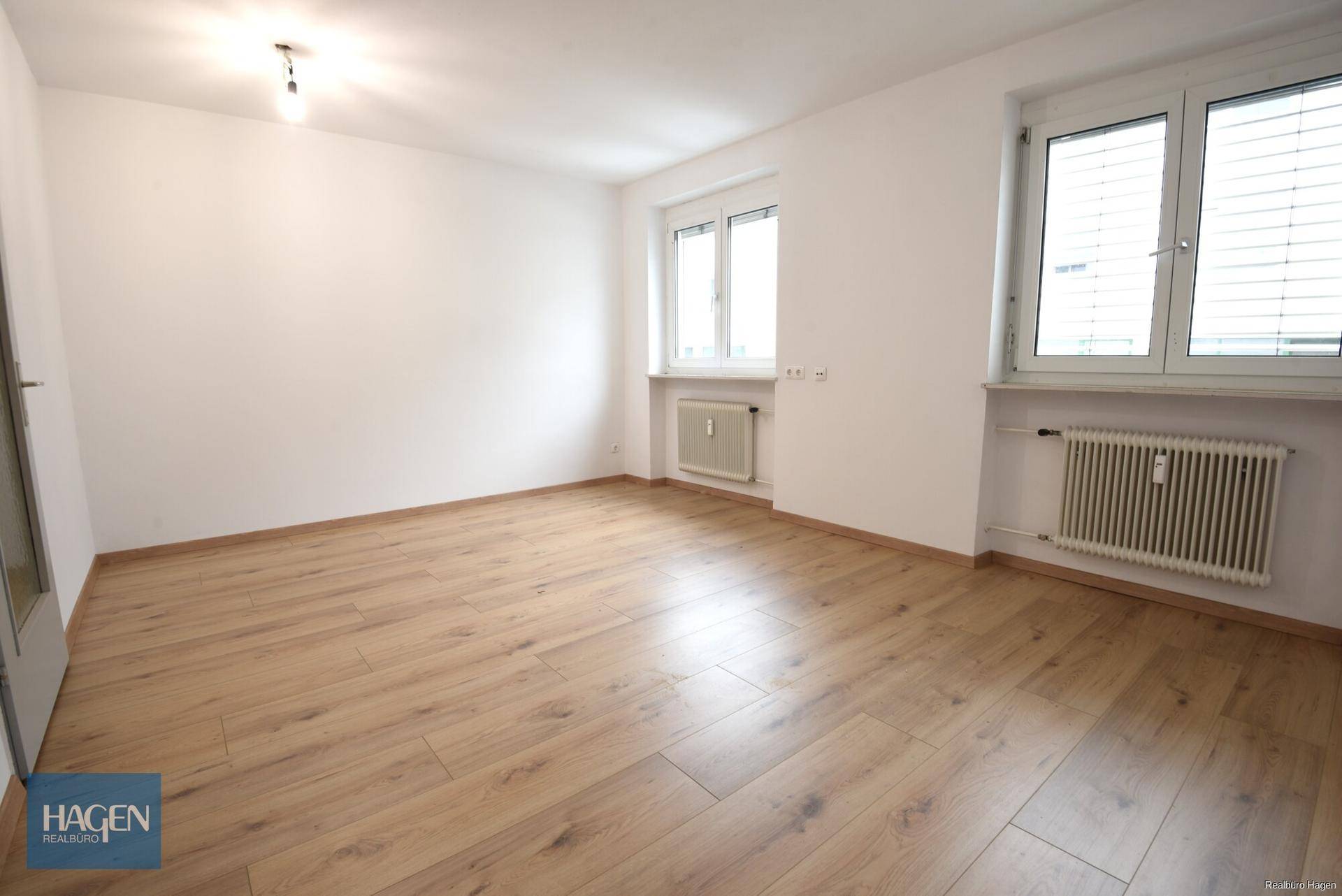 Großzügiges Zimmer mit hellem Laminatboden und zwei Fenstern, bietet vielseitige Nutzungsmöglichkeiten.