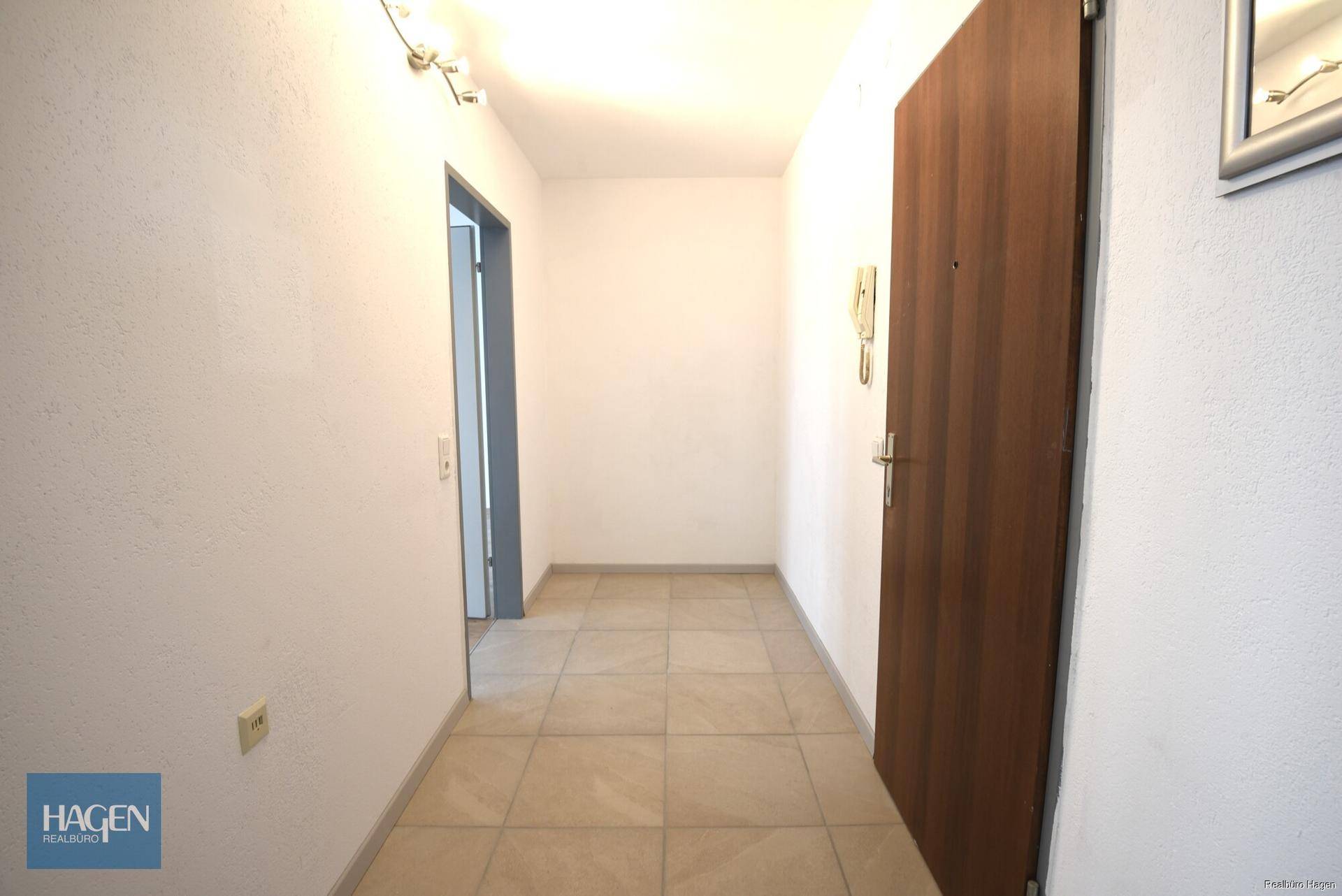Heller Eingangsbereich mit Fliesenboden und einer robusten Holztür, führt zu den Wohnräumen.