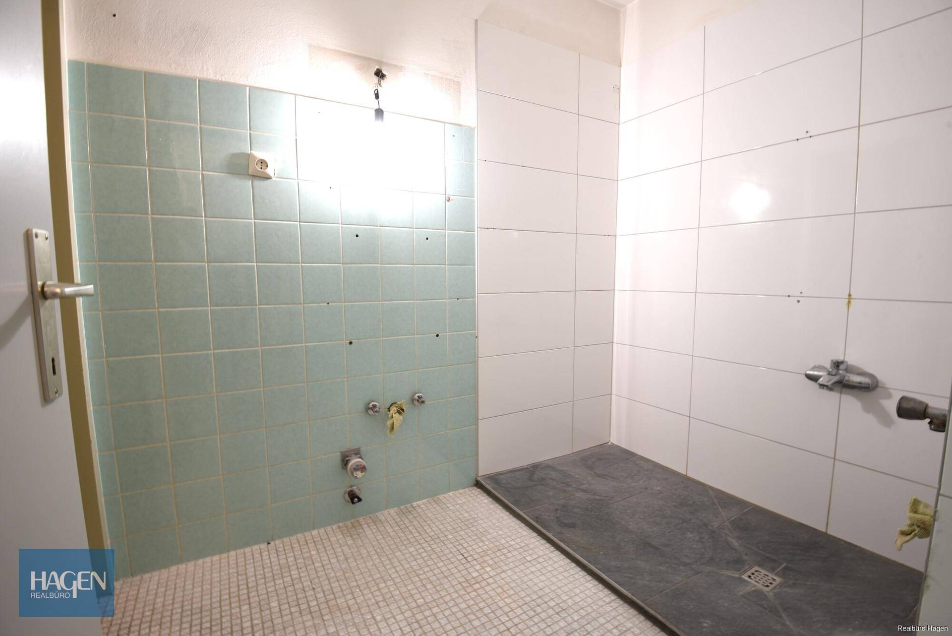 Badezimmer in originalem Zustand mit grünen und weißen Fliesen, bereit für eine Modernisierung.