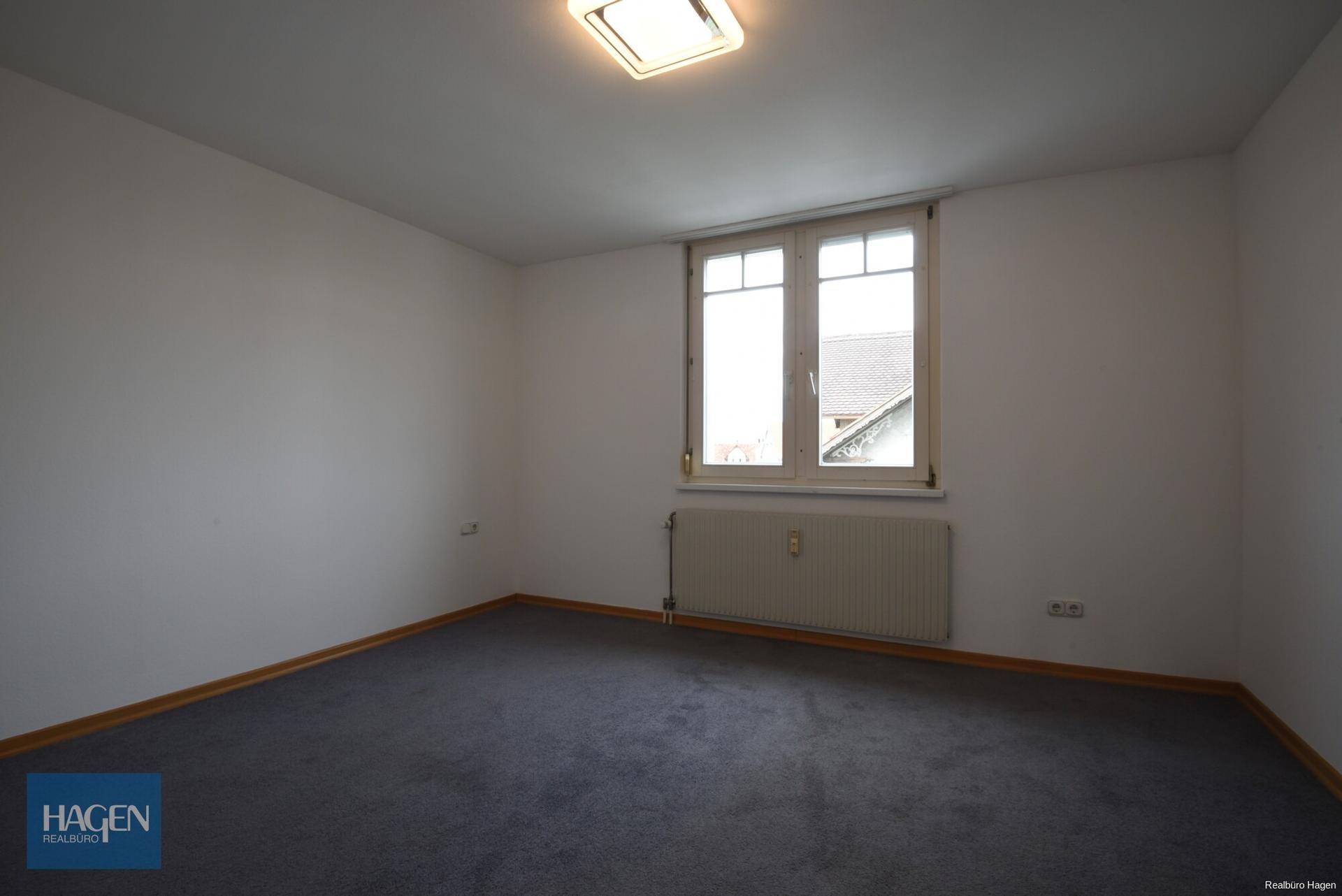 Ruhiges Schlafzimmer mit grauem Teppichboden und einem großen Fenster für natürliche Belichtung.