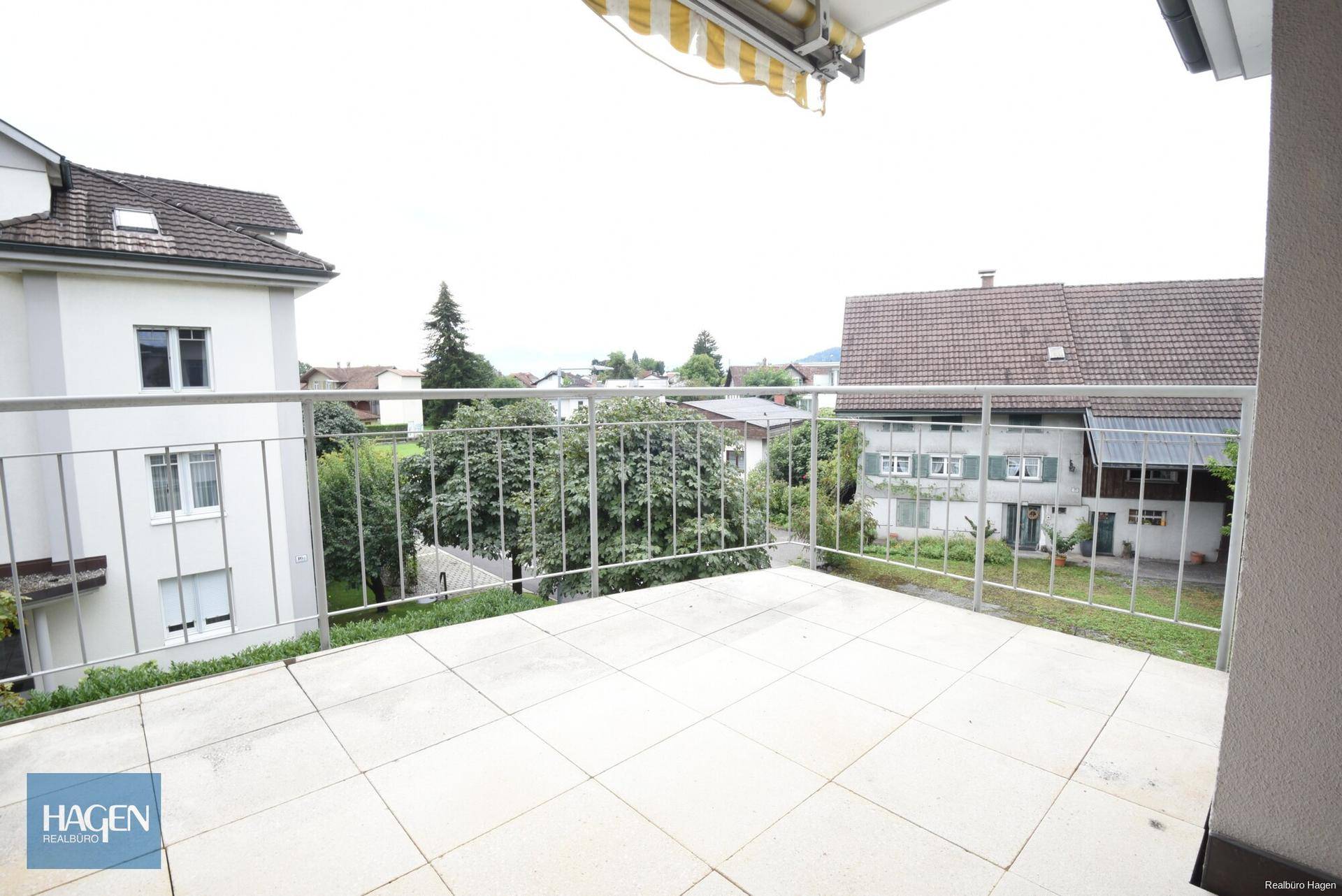 Geräumiger Balkon mit Fliesenboden und Blick auf die umliegende Wohngegend und Bäume.