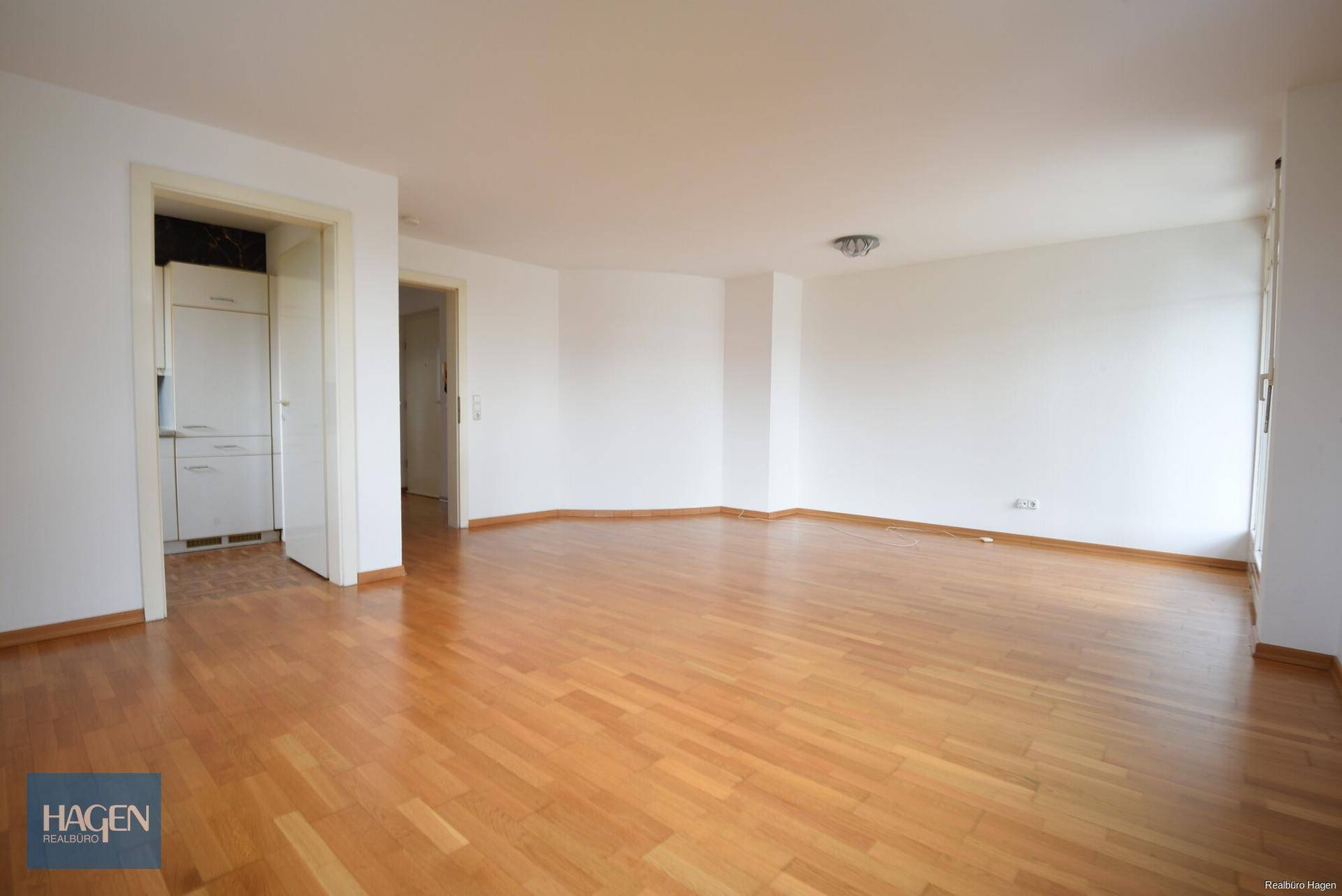 Heller Wohnbereich mit Holzparkett und offenem Zugang zu einem weiteren Raum oder Flur.