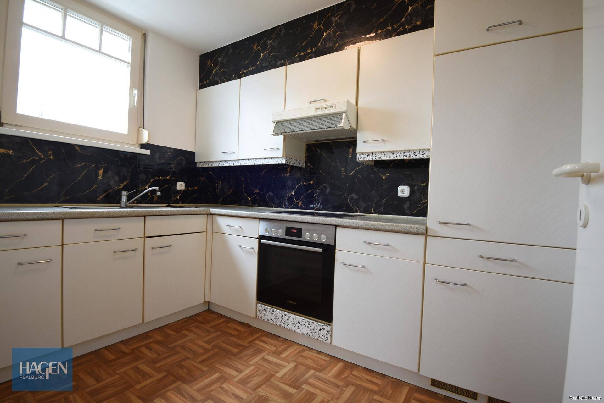Funktionale Küche mit weißen Schränken, dunkler Marmoroptik-Rückwand und integriertem Backofen.
