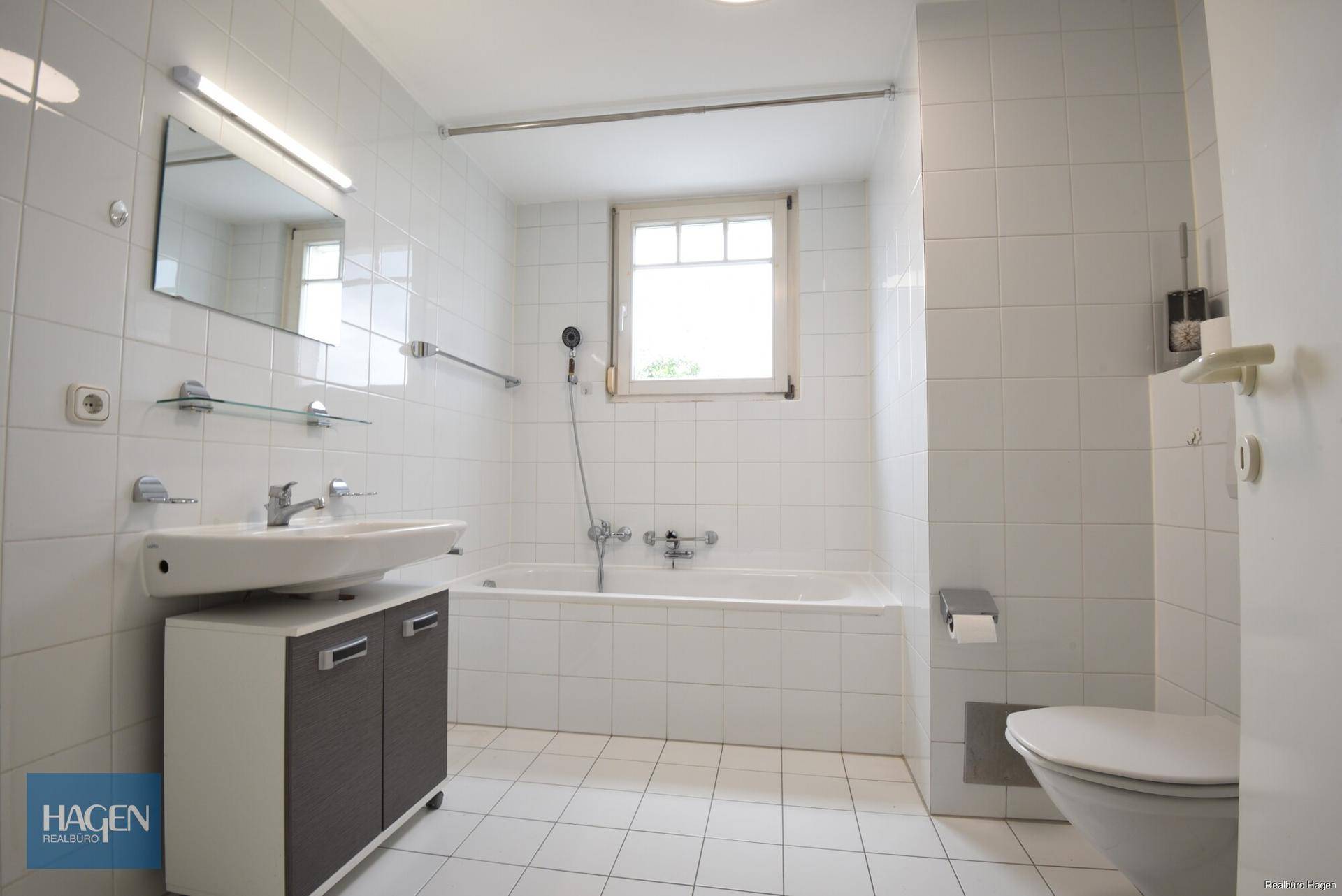 Gefliestes Badezimmer mit Badewanne, Waschbecken, Toilette und einem Fenster für Tageslicht.