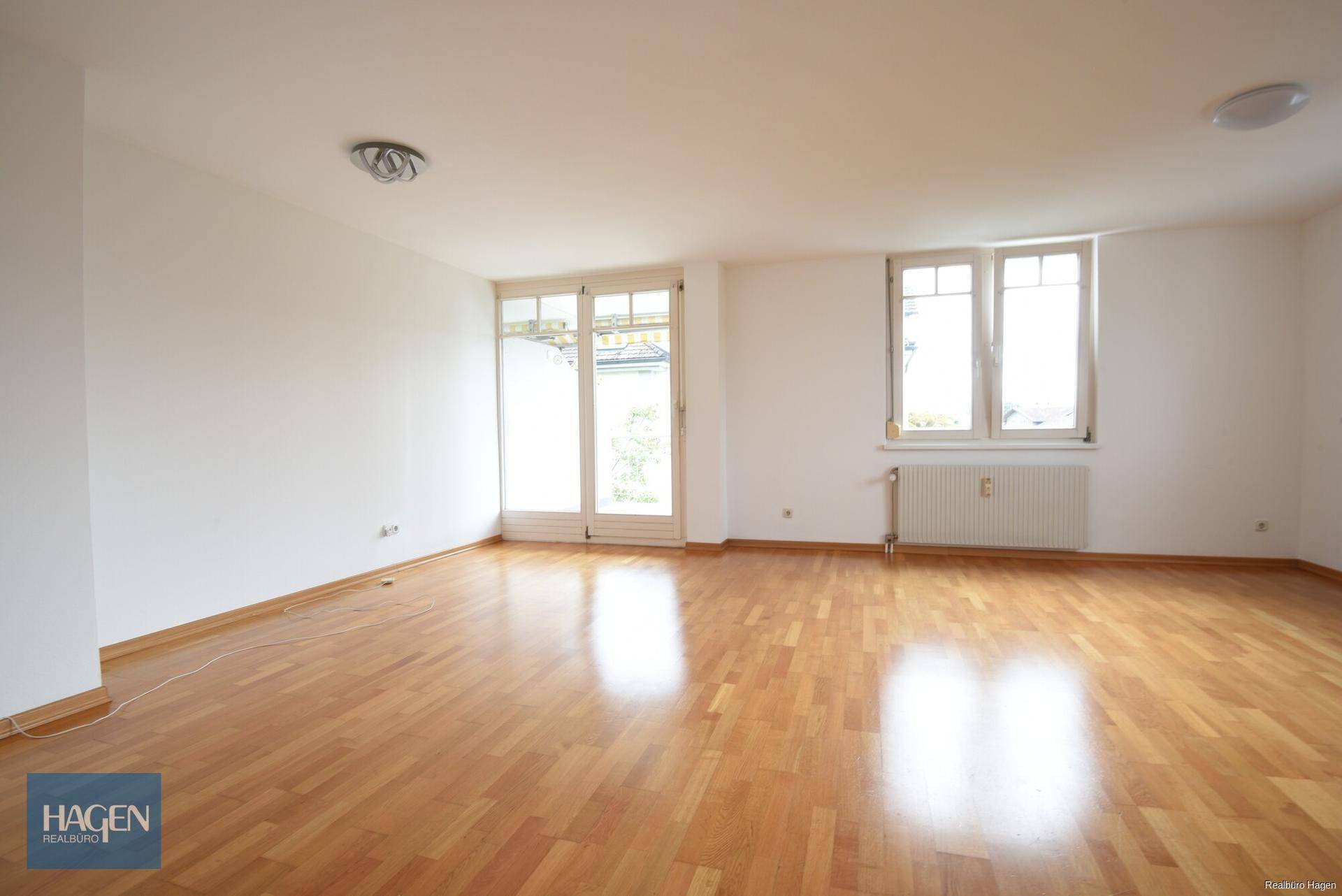 Helles Wohnzimmer mit Parkettboden, großen Fenstern und Zugang zu einem Balkon.