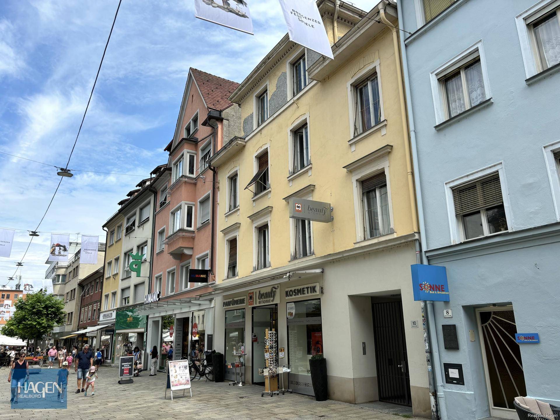 Blick auf eine belebte Einkaufsstraße mit historischen Gebäuden und Geschäften unter blauem Himmel.