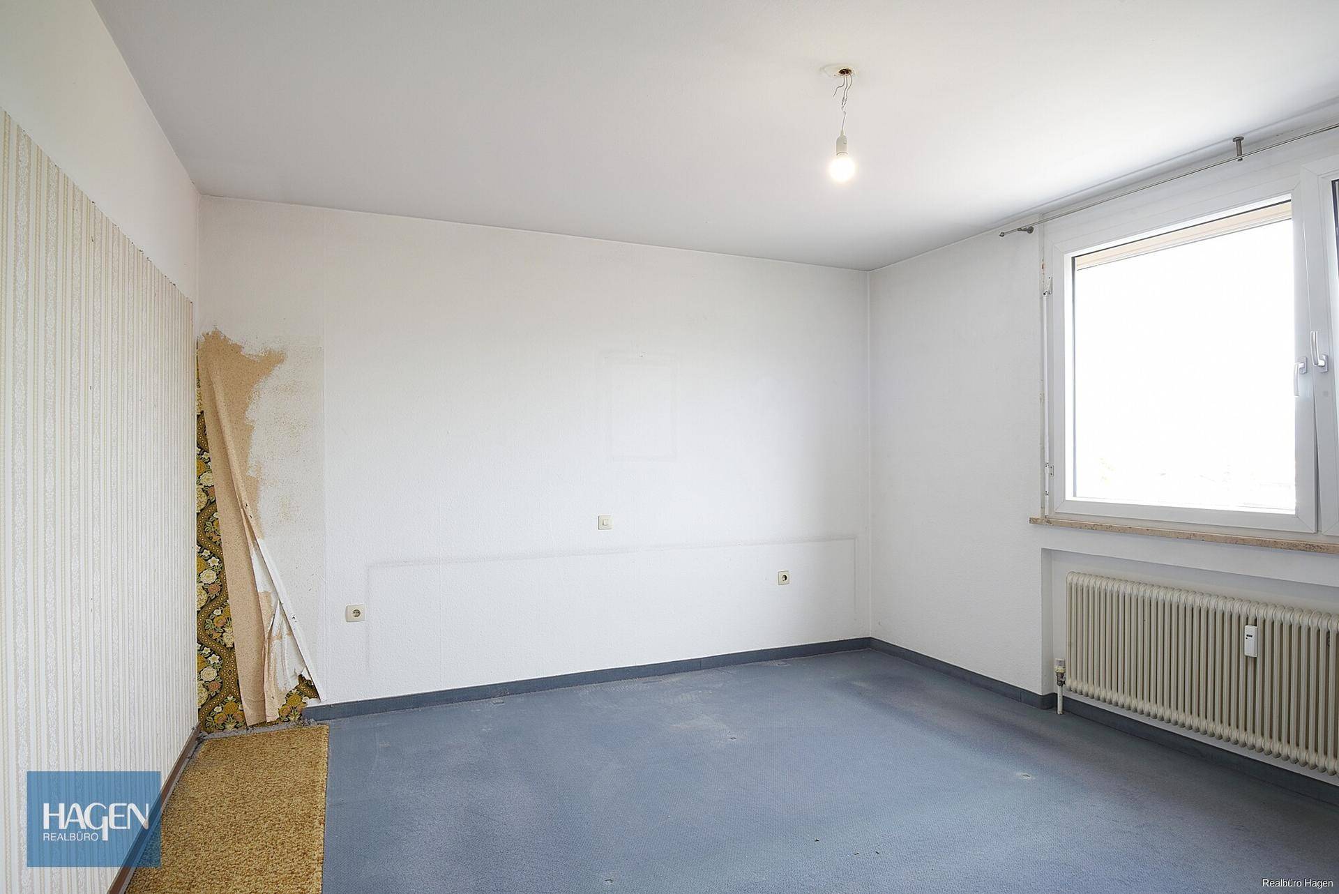 Leeres Zimmer mit Teppichboden und teilweise entfernter Tapete.