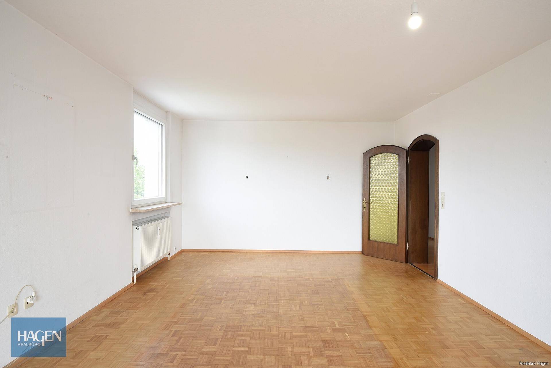 Helles, leeres Wohnzimmer mit Parkettboden und einer Doppeltür.