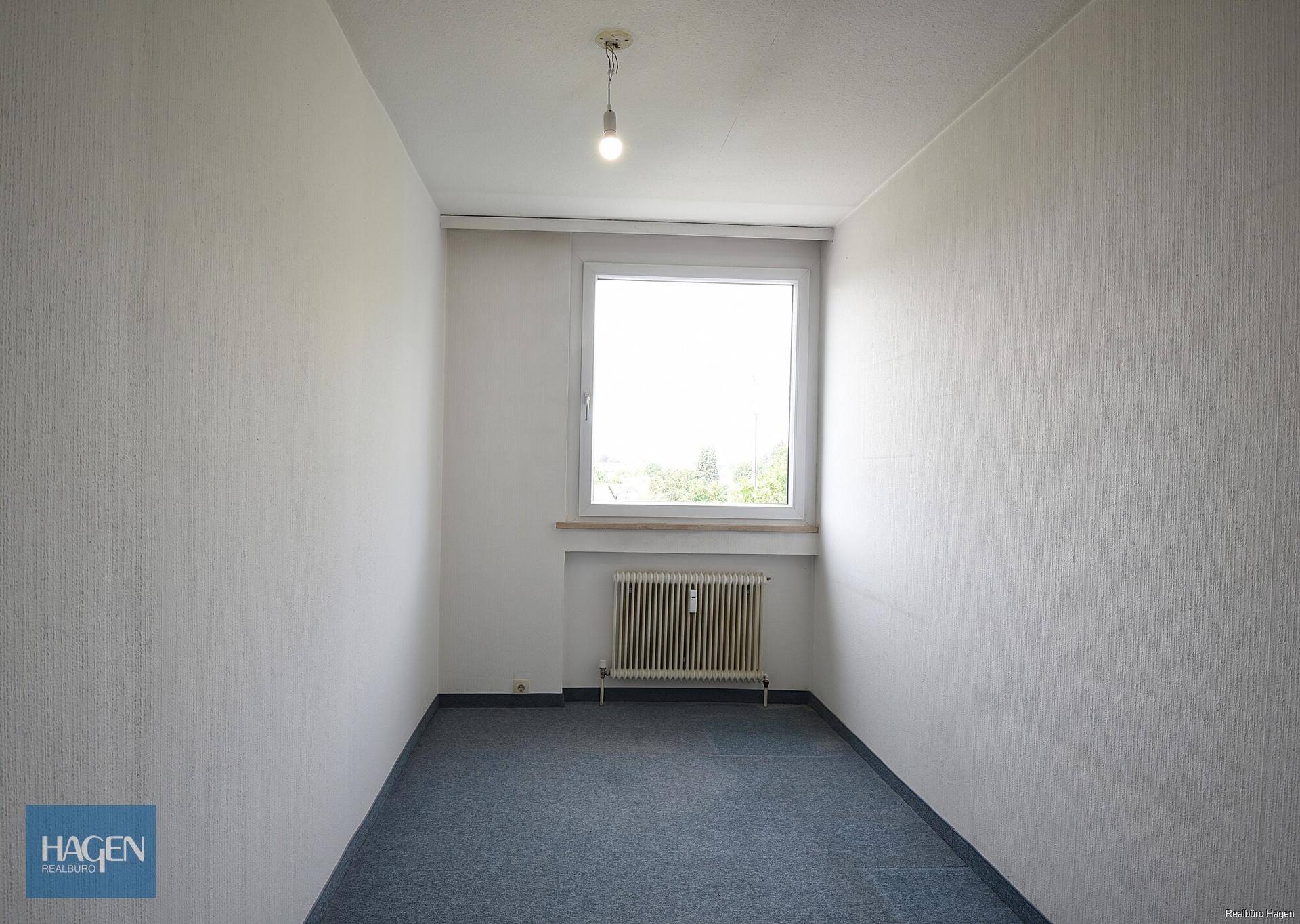 Kleines, leeres Zimmer mit Teppichboden und einem Fenster.