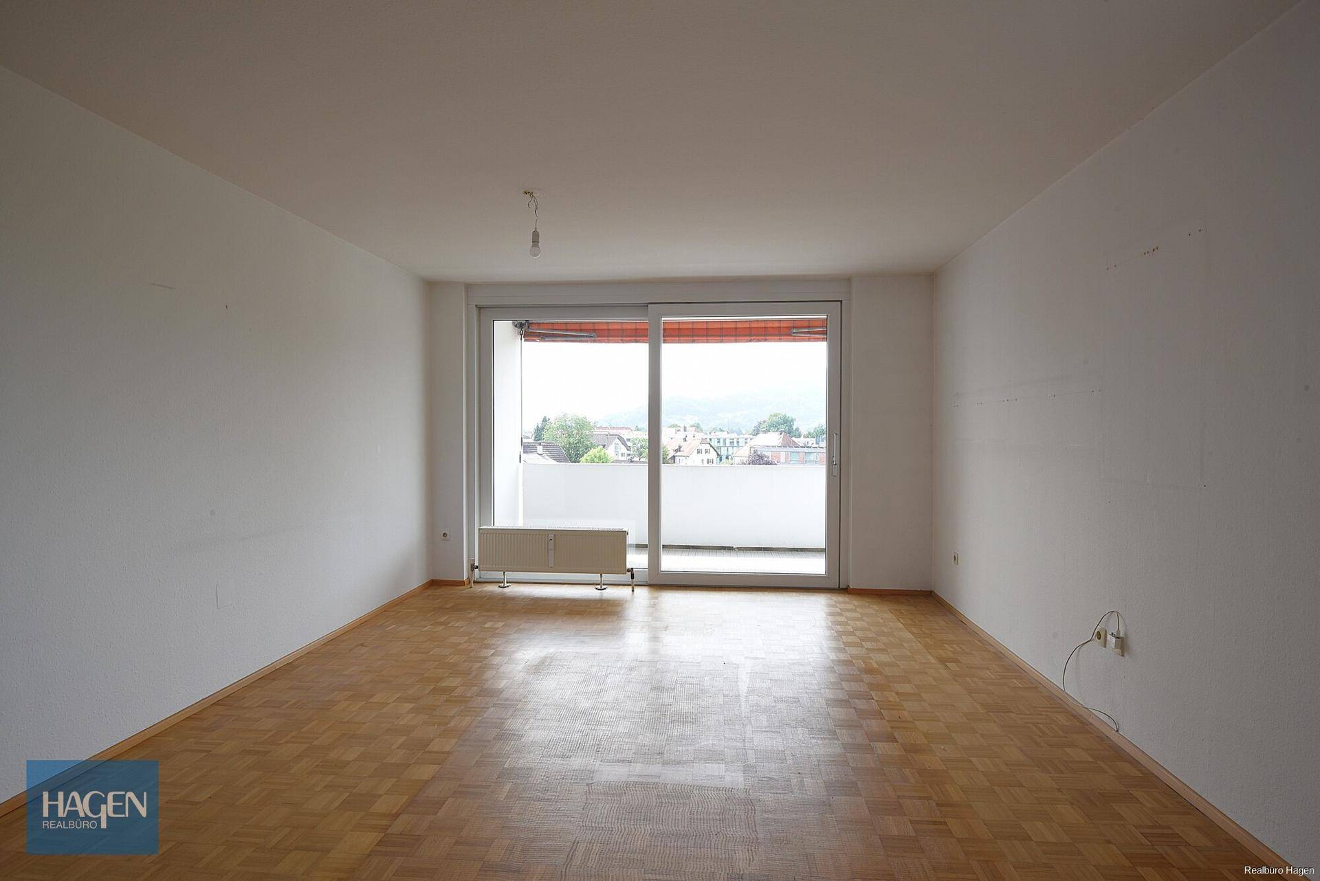 Geräumiges Wohnzimmer mit Parkettboden und Zugang zu einem sonnigen Balkon.