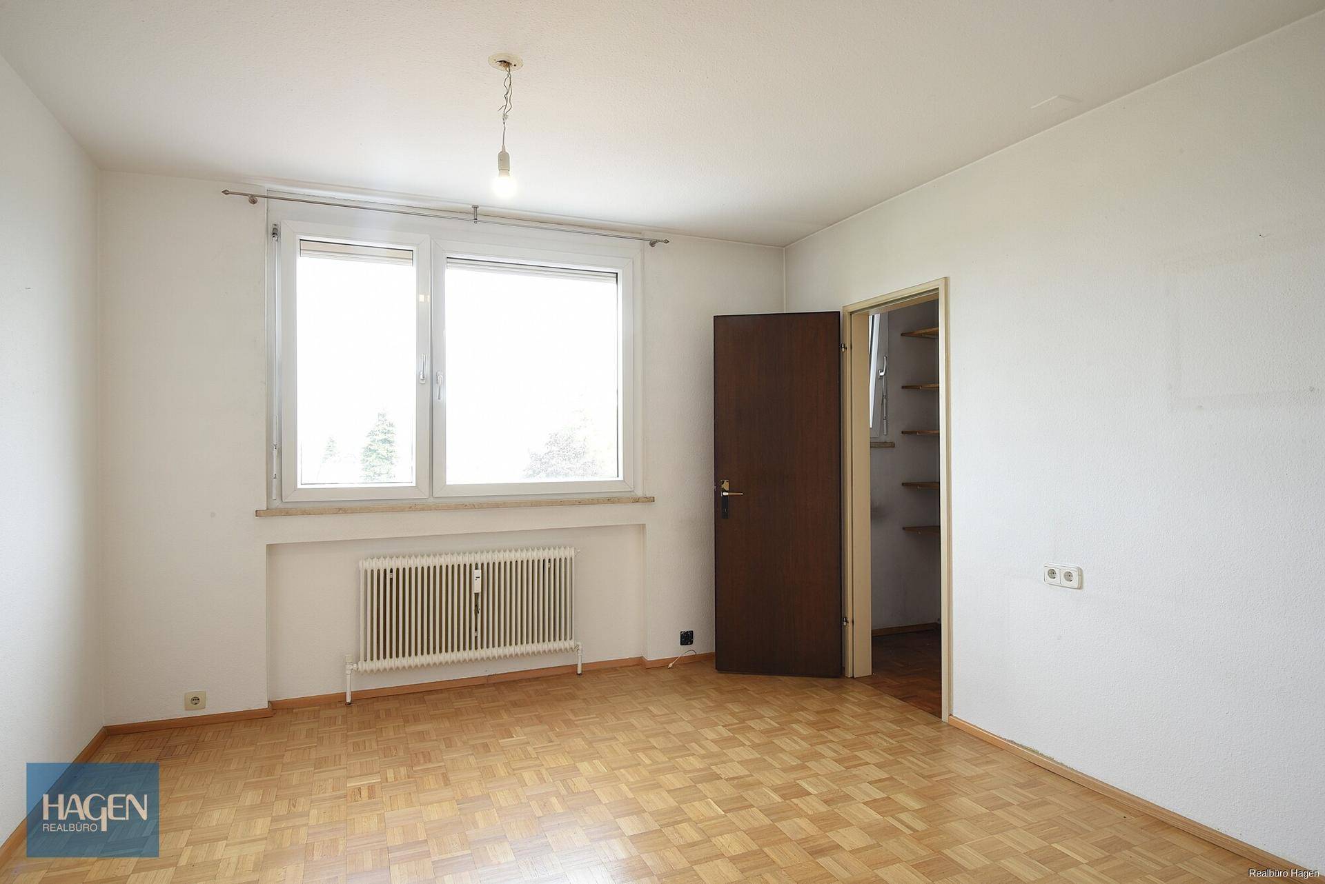Helles Schlafzimmer mit Parkettboden, großem Fenster und Heizkörper.