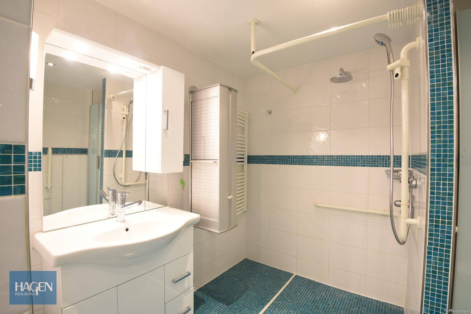 Modernes Badezimmer mit barrierefreier Dusche, blauen Akzentfliesen und Haltegriffen.