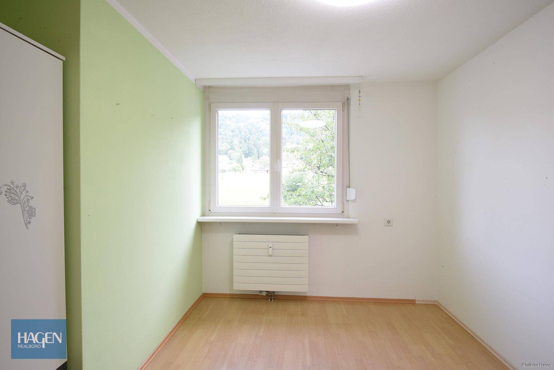 Helles Schlafzimmer mit grün akzentuierter Wand und Blick ins Grüne.
