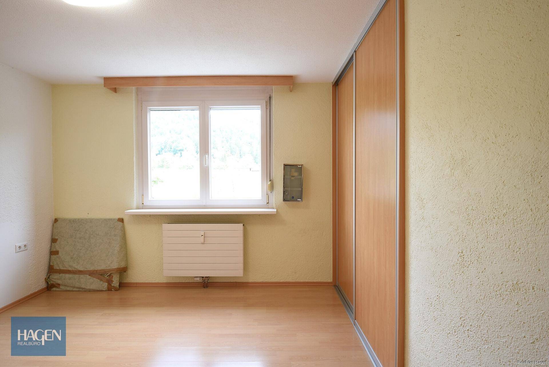 Schlafzimmer mit hellem Laminatboden, Fenster und integriertem Kleiderschrank.