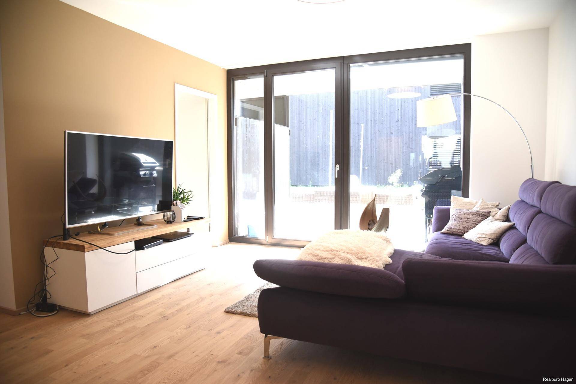 Gemütliches Wohnzimmer mit Sofa, Fernseher und großen Fenstern zum Terrassenzugang.