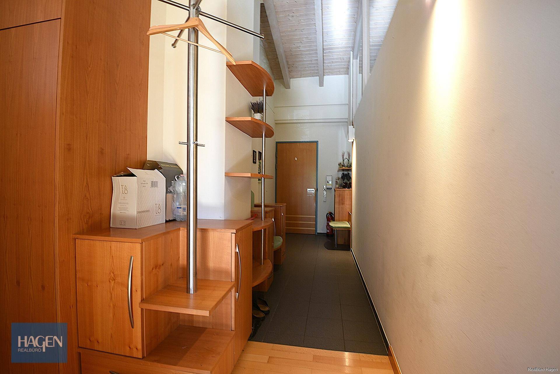 Heller Eingangsbereich mit Holzmöbeln, Garderobe und sichtbaren Dachbalken.