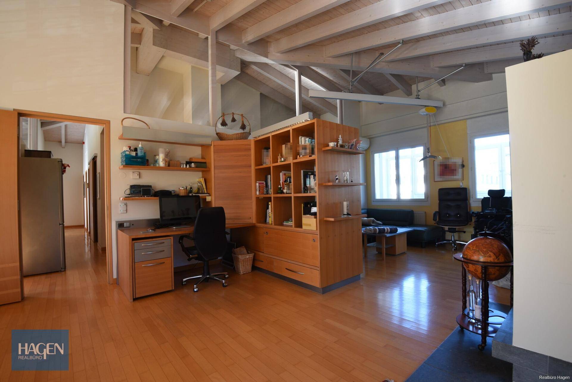 Offener Arbeitsbereich mit Schreibtisch, Bücherregal und Blick in den Wohnbereich.