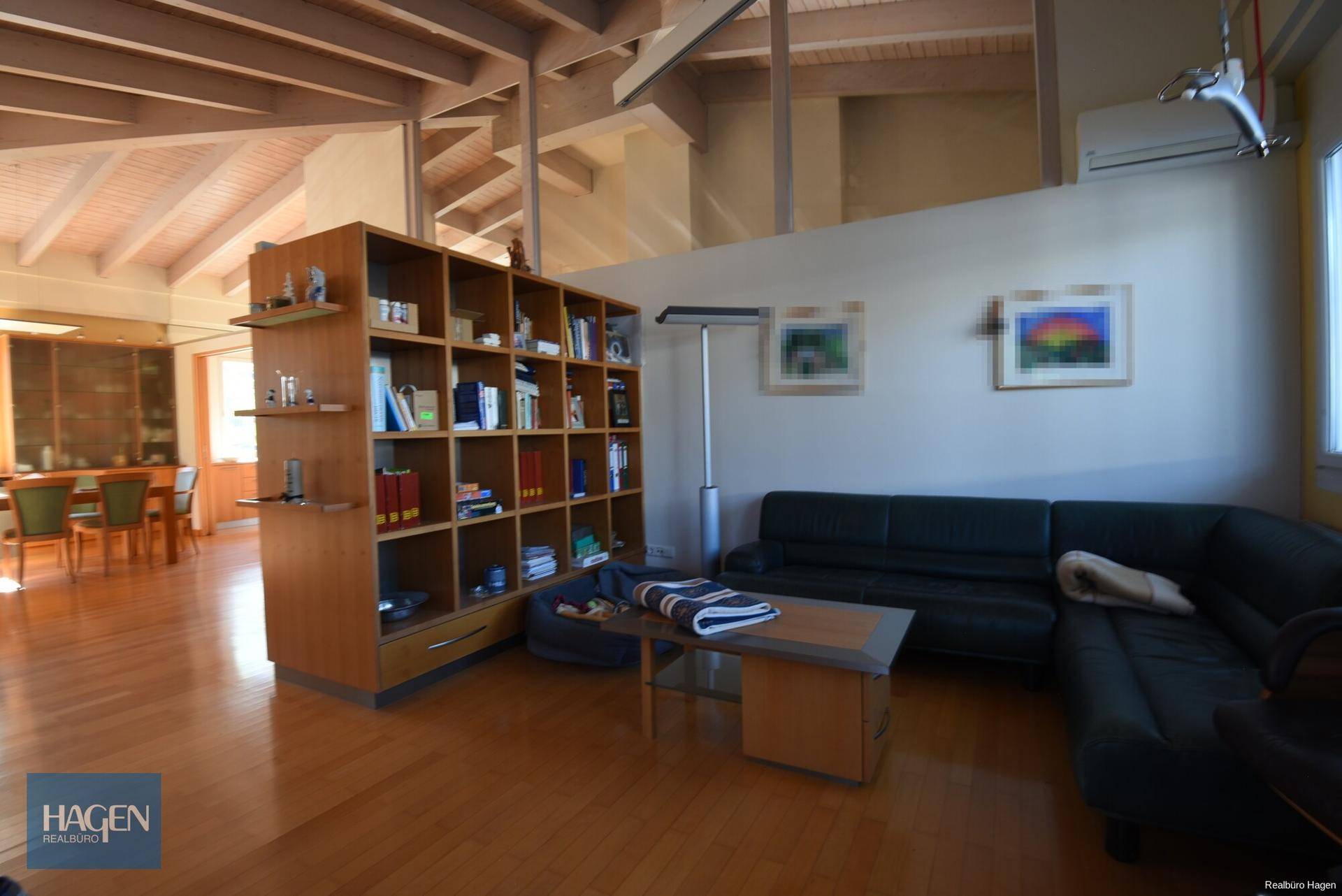 Gemütlicher Wohnbereich mit Ledersofa, Bücherregal und Holzboden unter hohen Decken.