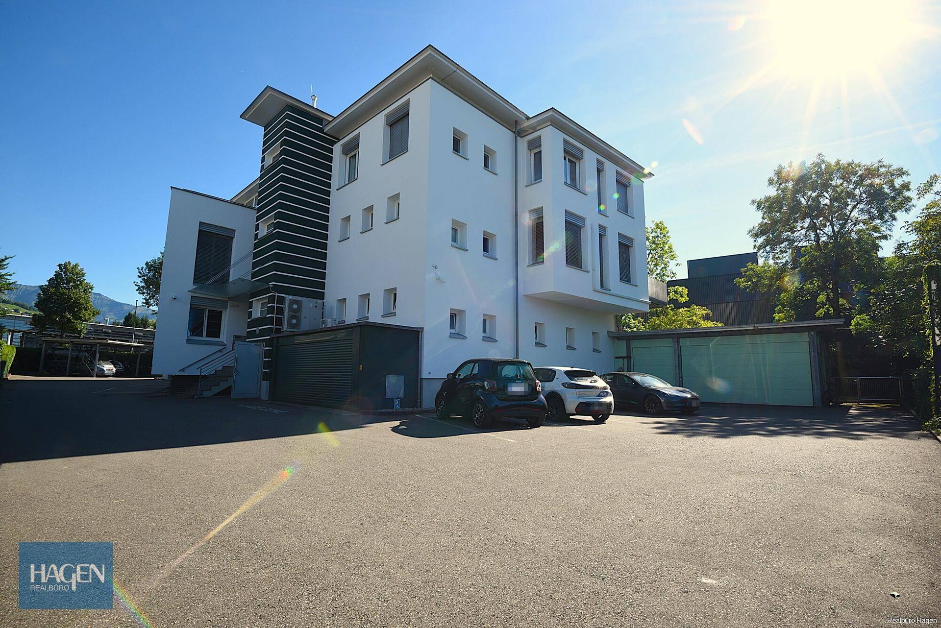 Modernes Mehrfamilienhaus mit Garagen und Außenparkplätzen unter blauem Himmel.