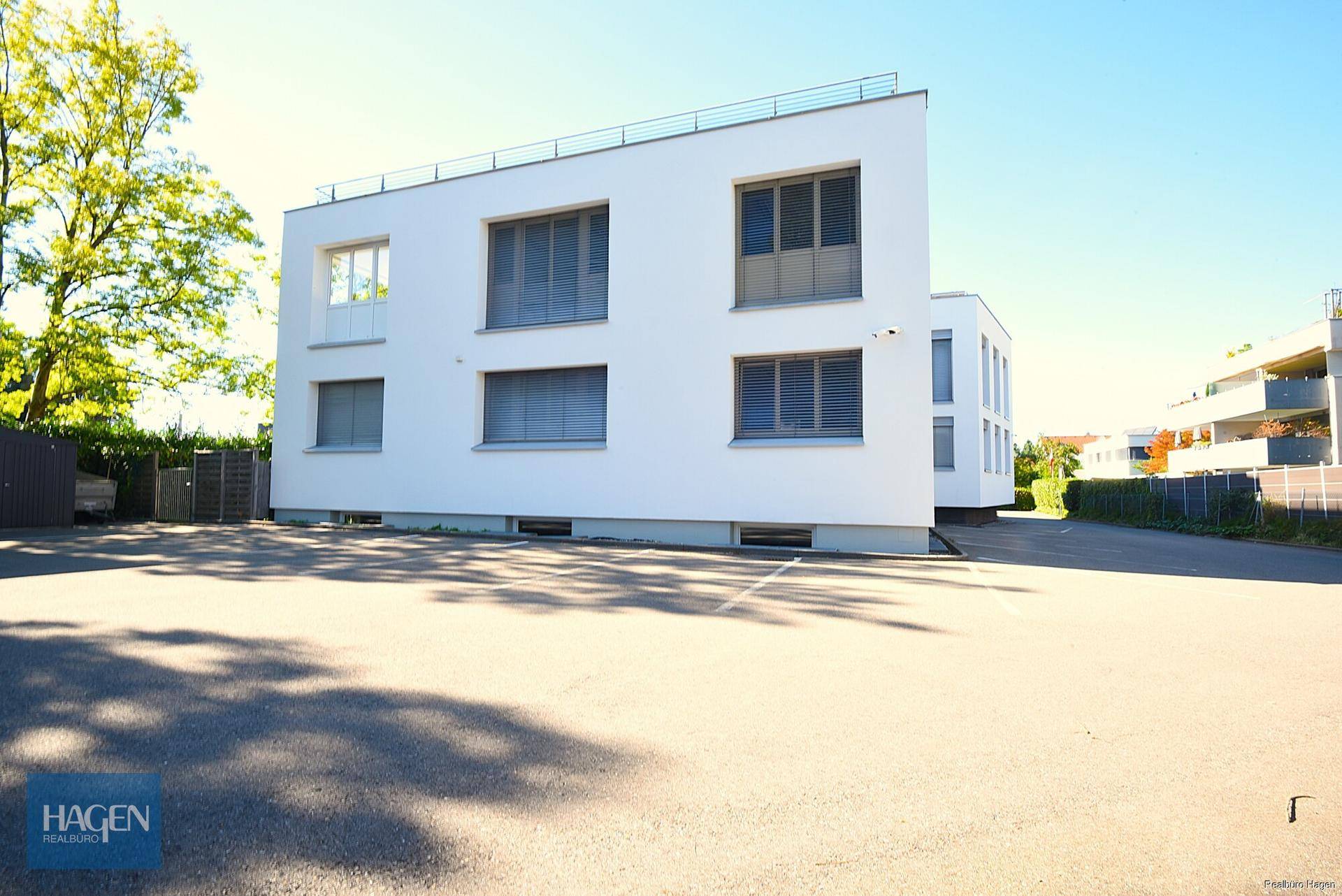 Moderne Wohnanlage mit weißer Fassade und großem Parkplatz im Freien.