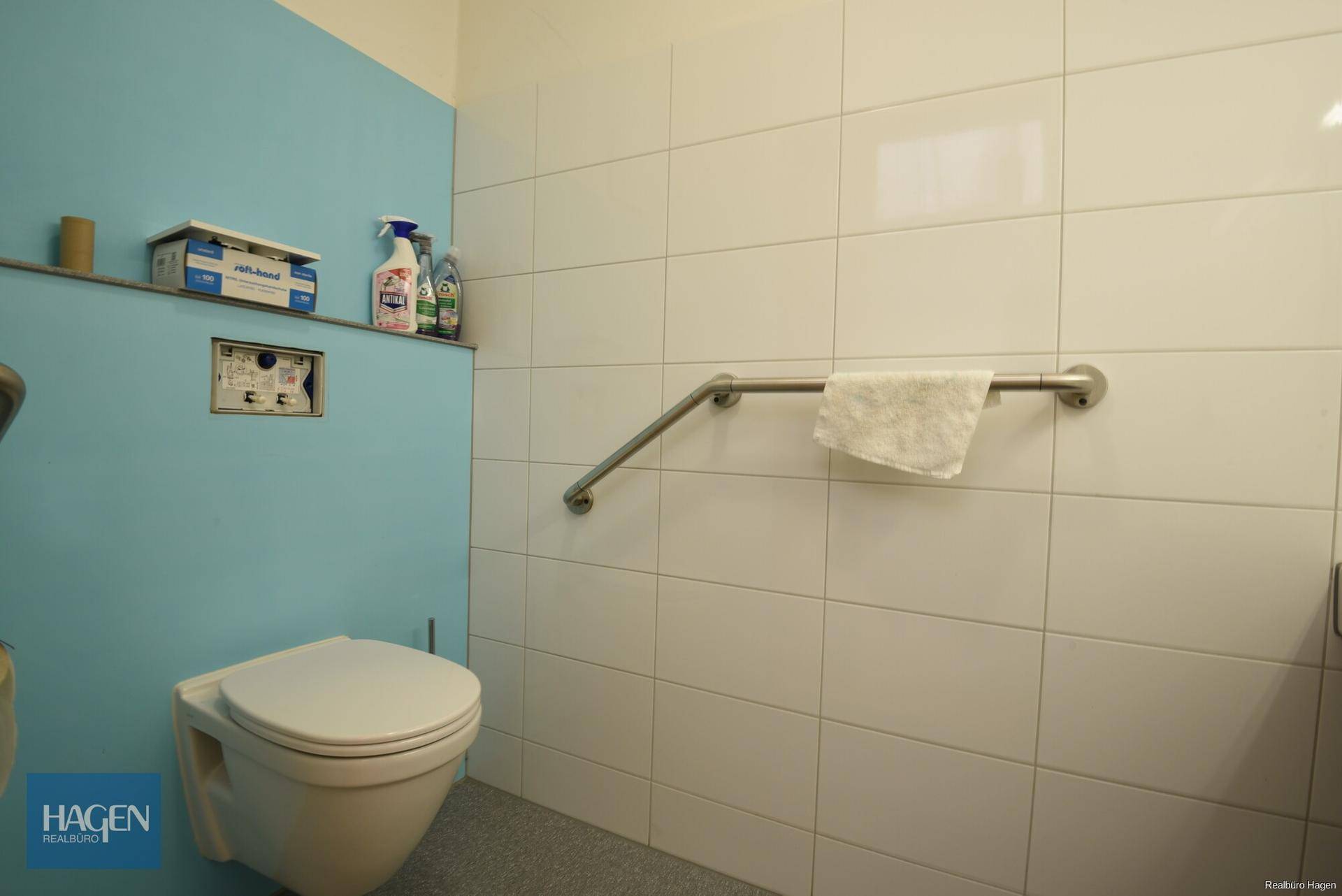 Barrierefreies WC mit Wand-WC und Haltegriffen an den Wänden.