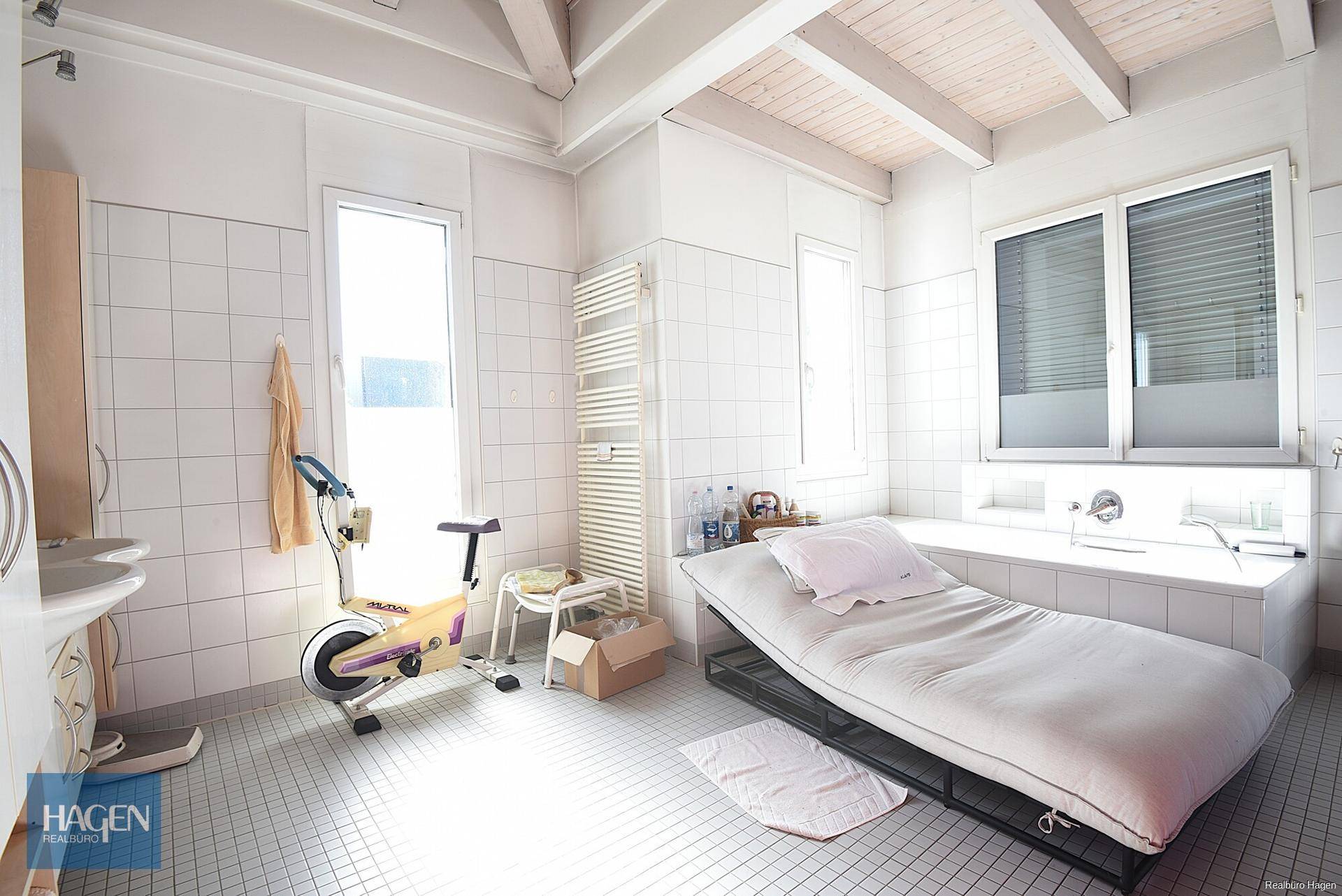 Geräumiges Badezimmer mit Badewanne, Fitnessgerät und hellen Fliesen.