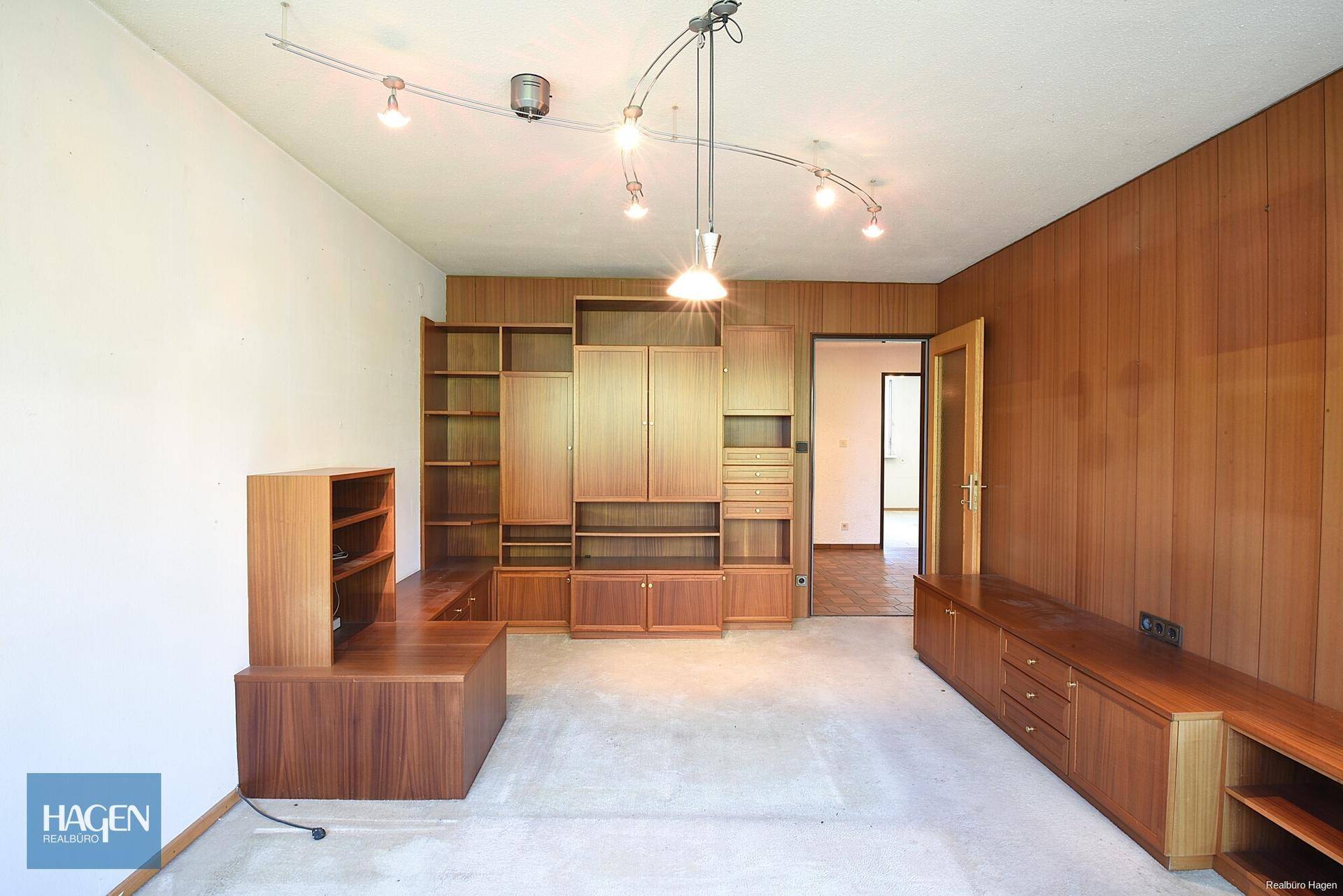 Geräumiges Wohnzimmer mit Holzwänden, Einbauschränken und Teppichboden, bietet viel Stauraum.