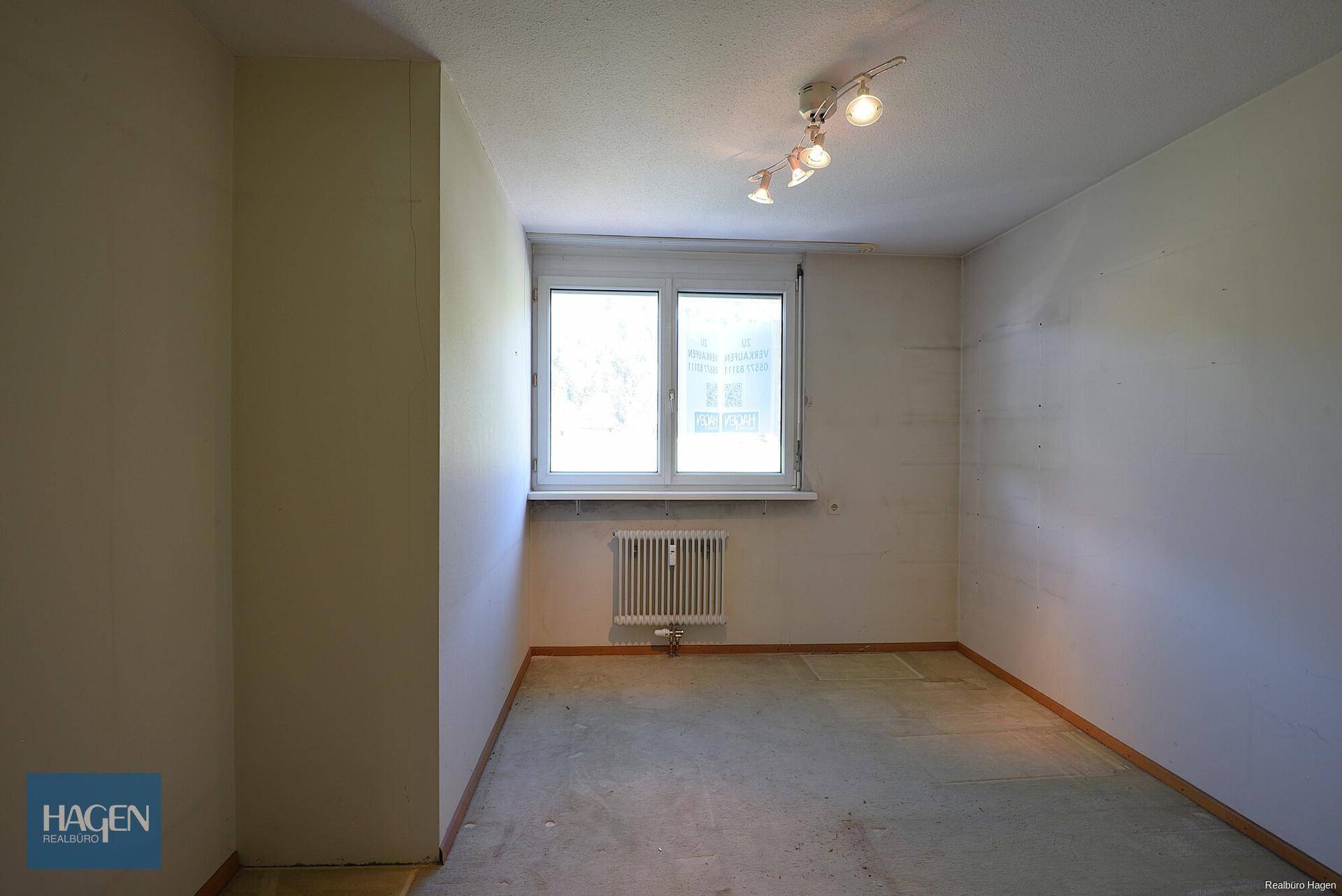 Helles Schlafzimmer mit Fenster, Heizkörper und Teppichboden, bereit zur individuellen Gestaltung.
