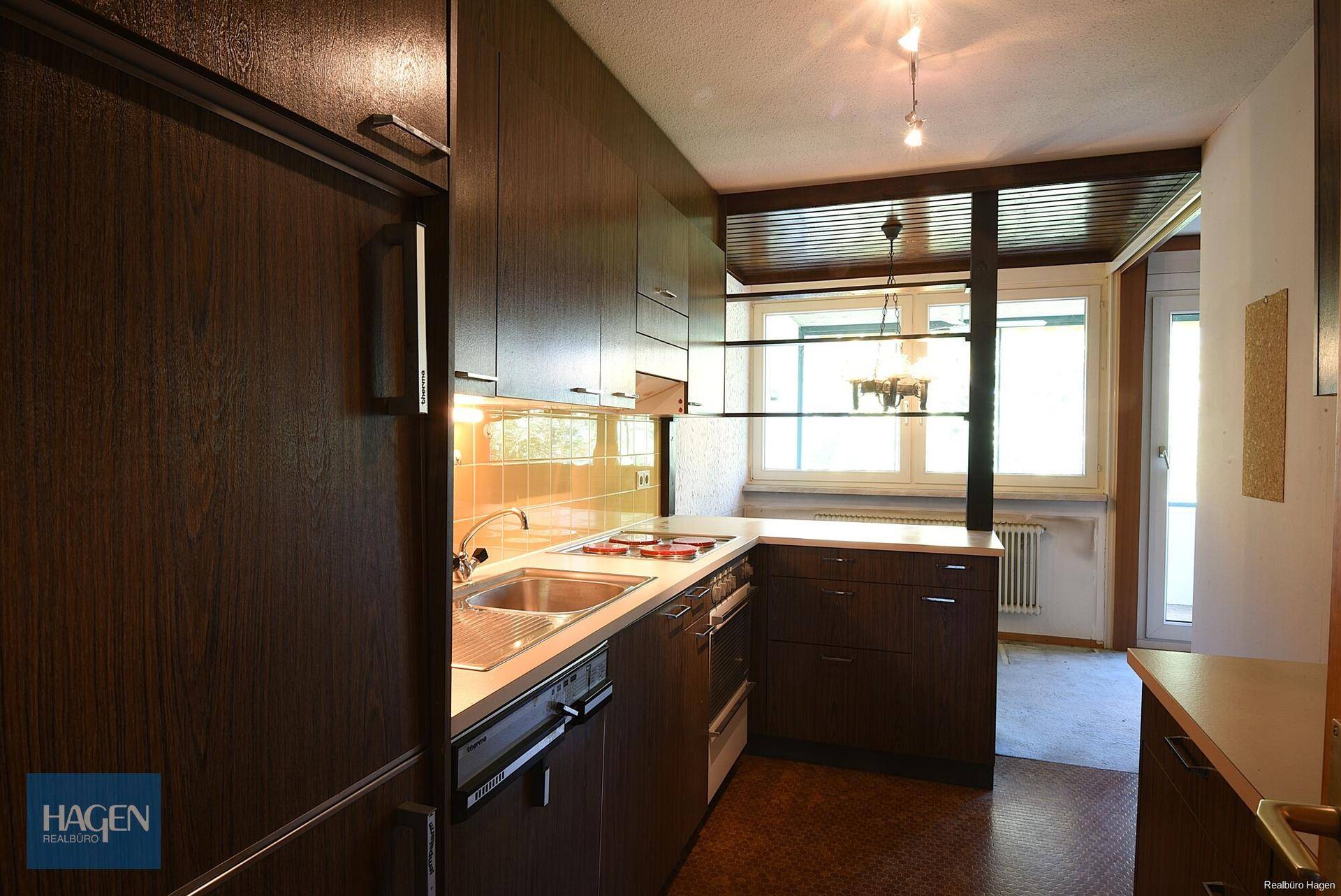 Funktionale Küche mit dunklen Holzschränken, integrierten Geräten und Fenster für Tageslicht.