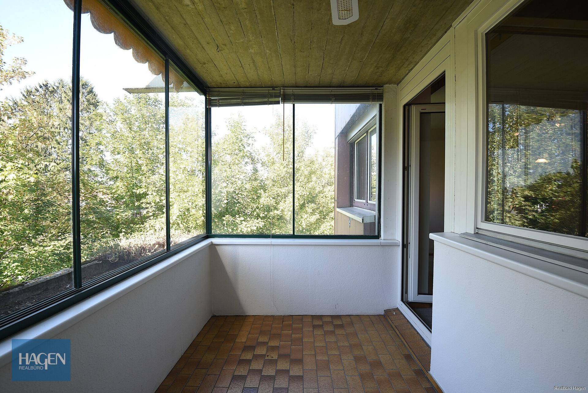 Verglaste Loggia mit Fliesenboden und Blick ins Grüne, ideal für entspannte Stunden im Freien.