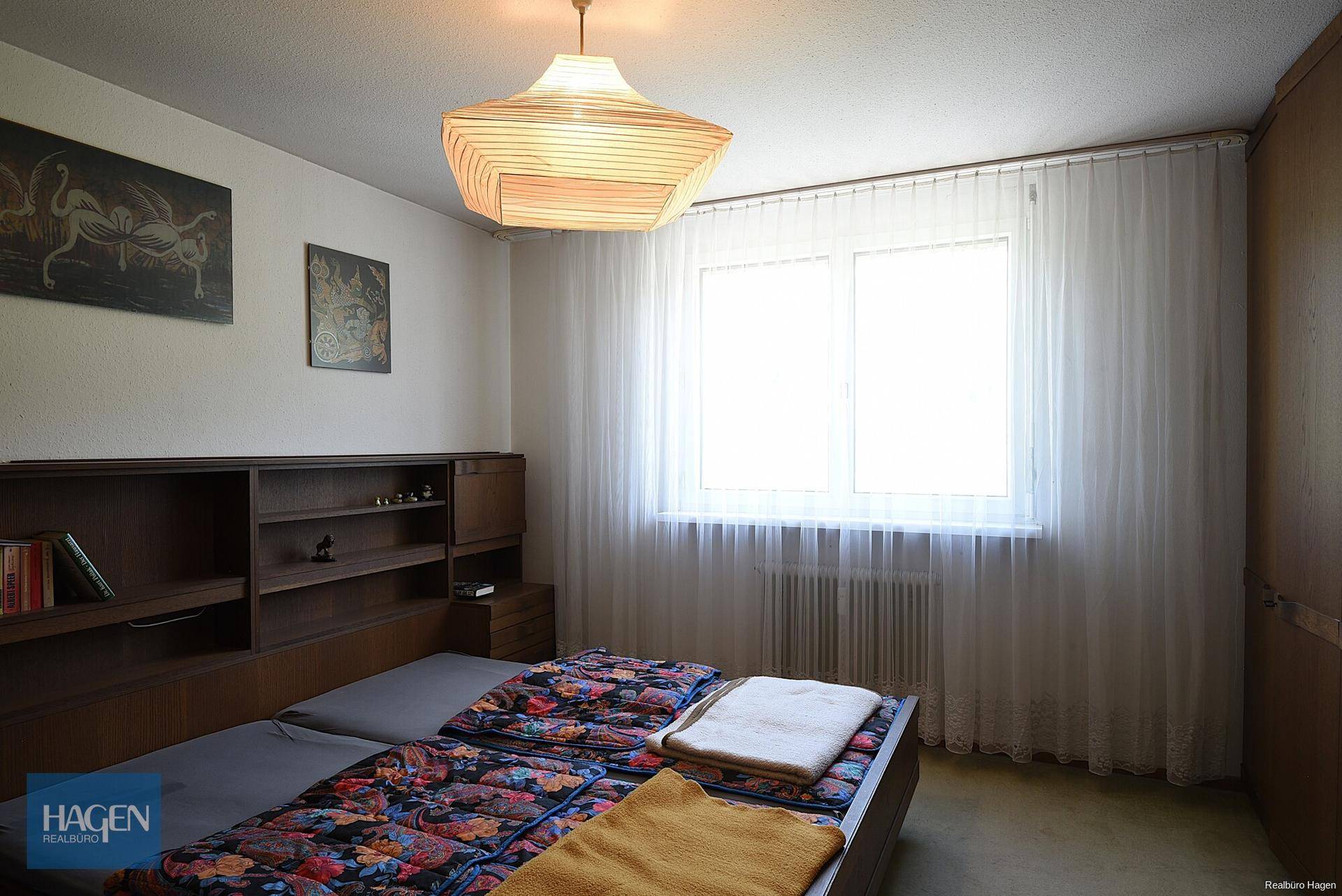 Gemütliches Schlafzimmer mit Doppelbett, Einbauregal und großem Fenster mit Vorhängen.