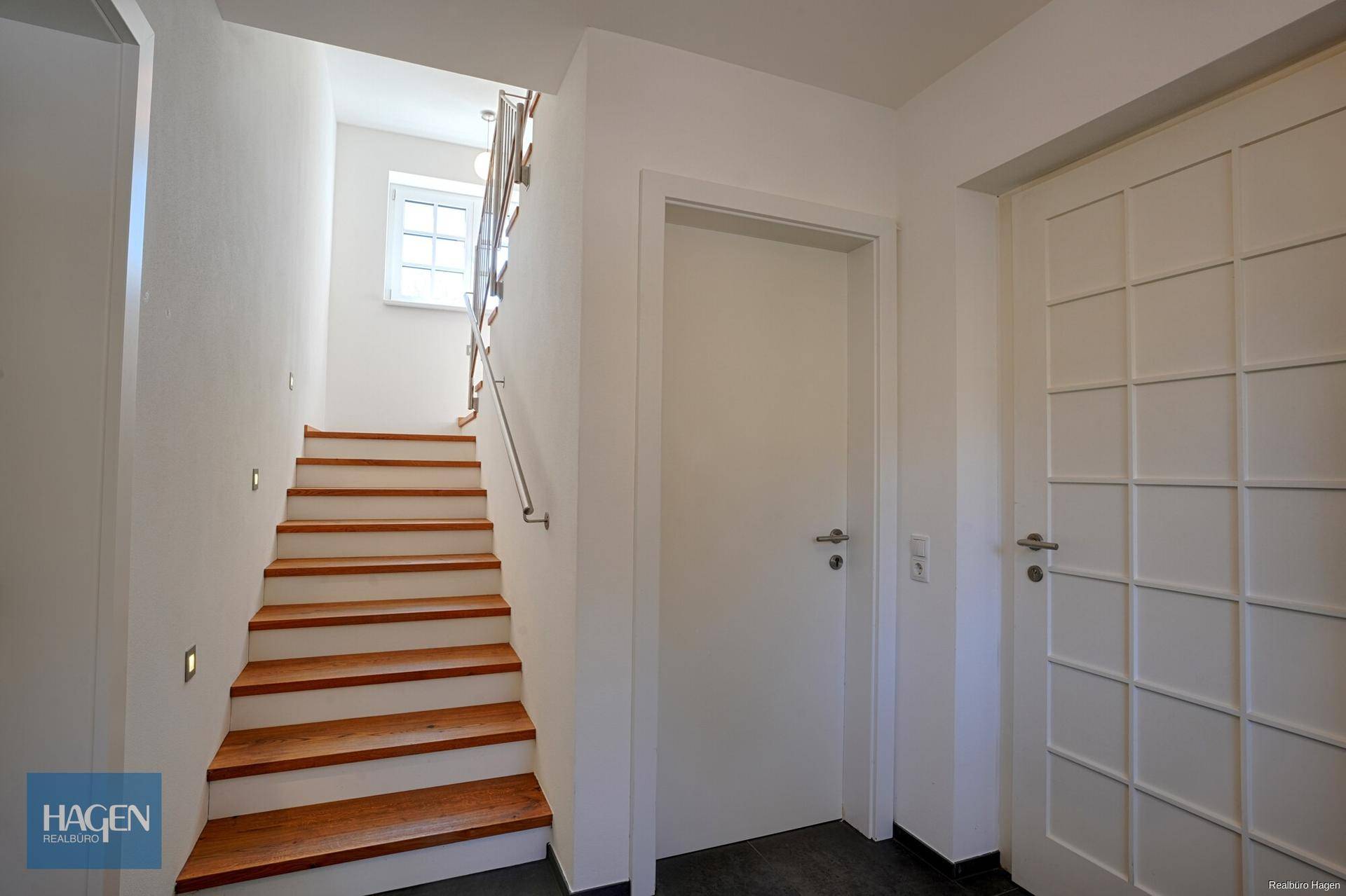 Heller Flur mit Holztreppe und modernen Einbaustrahlern, der zu den oberen Etagen führt.
