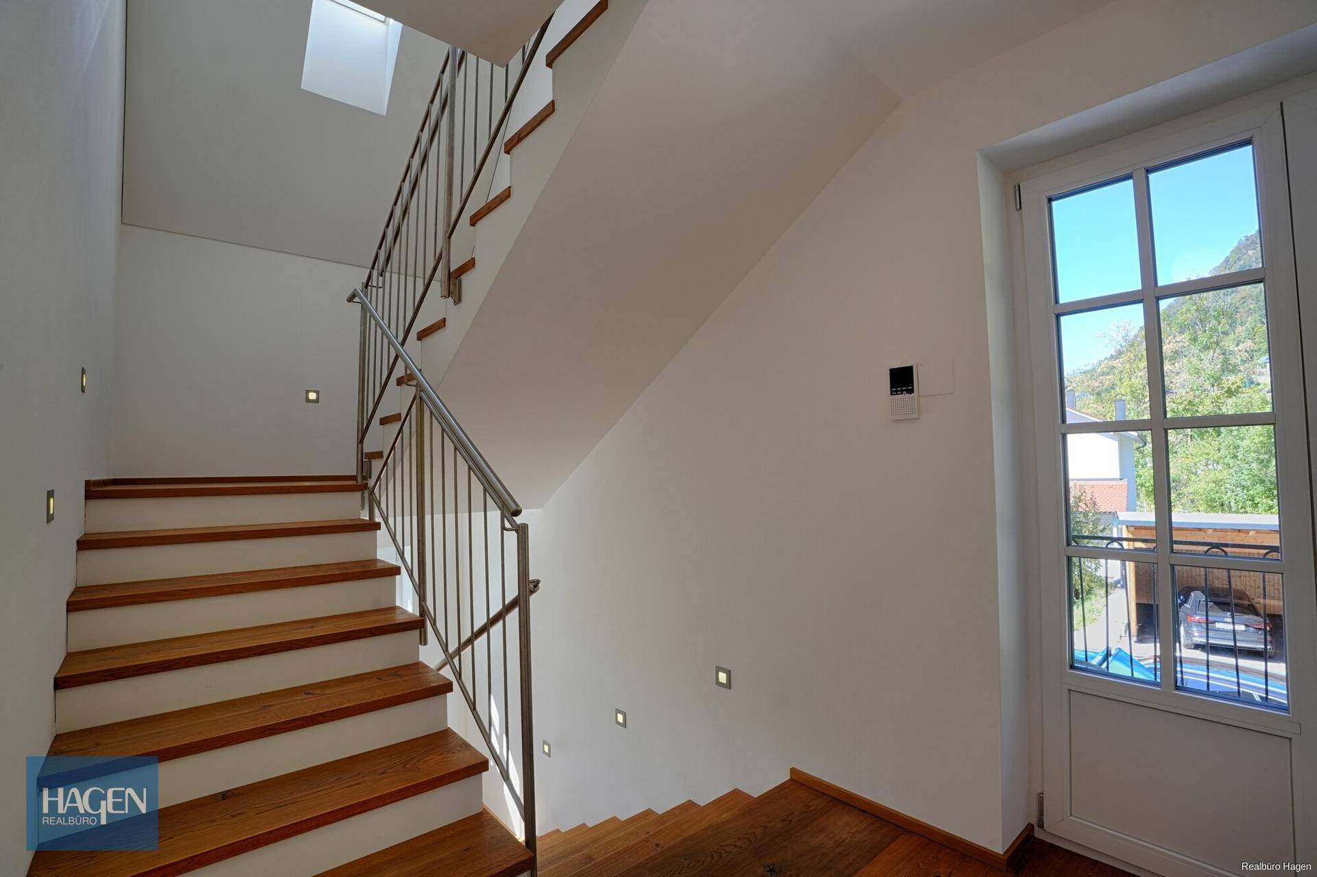 Moderne Holztreppe mit Edelstahlgeländer und integrierter Beleuchtung, die das Obergeschoss erschließt.