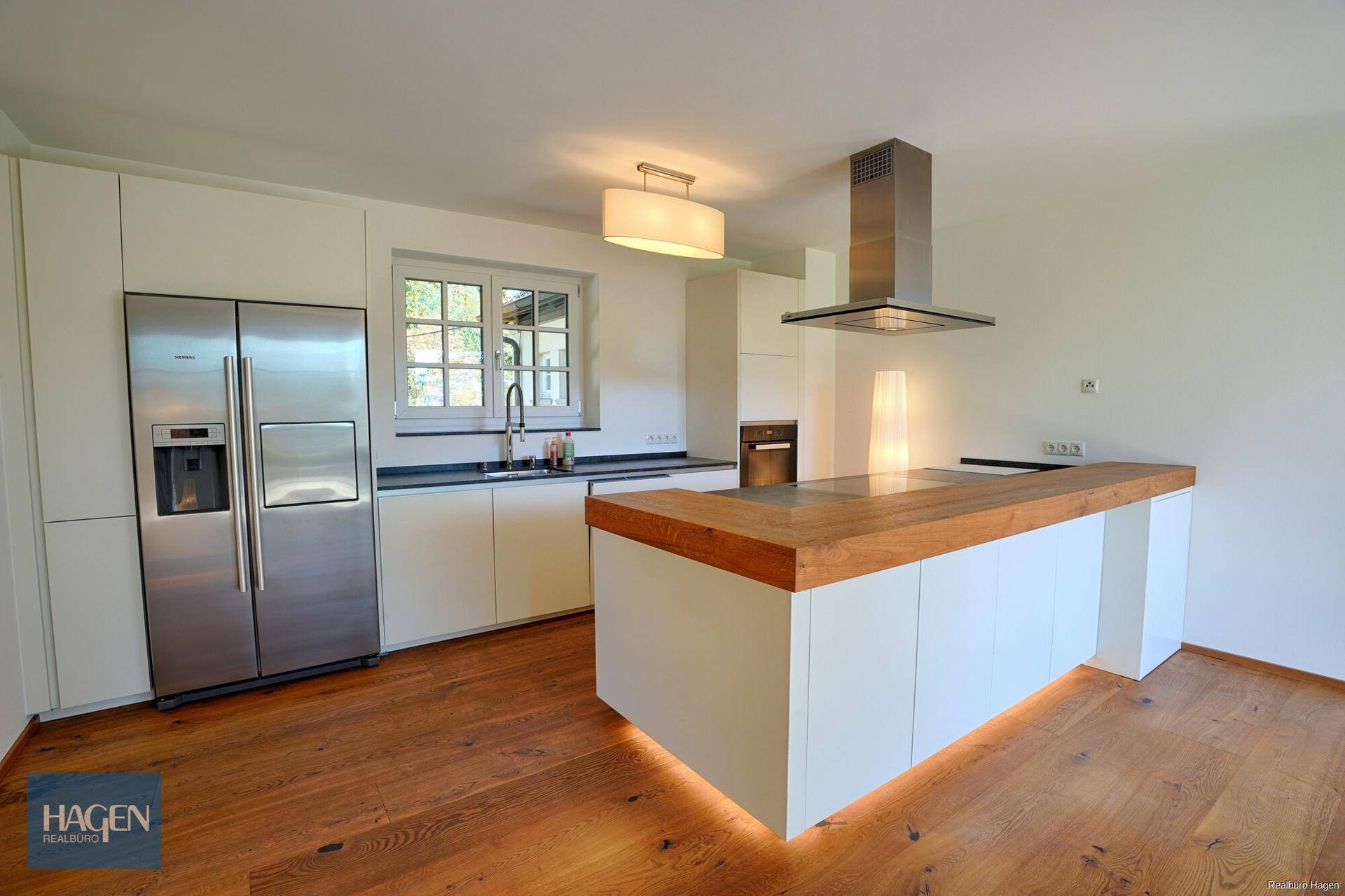 Moderne Küche mit weißer Front, Holztheke, großem Kühlschrank und Holzboden.