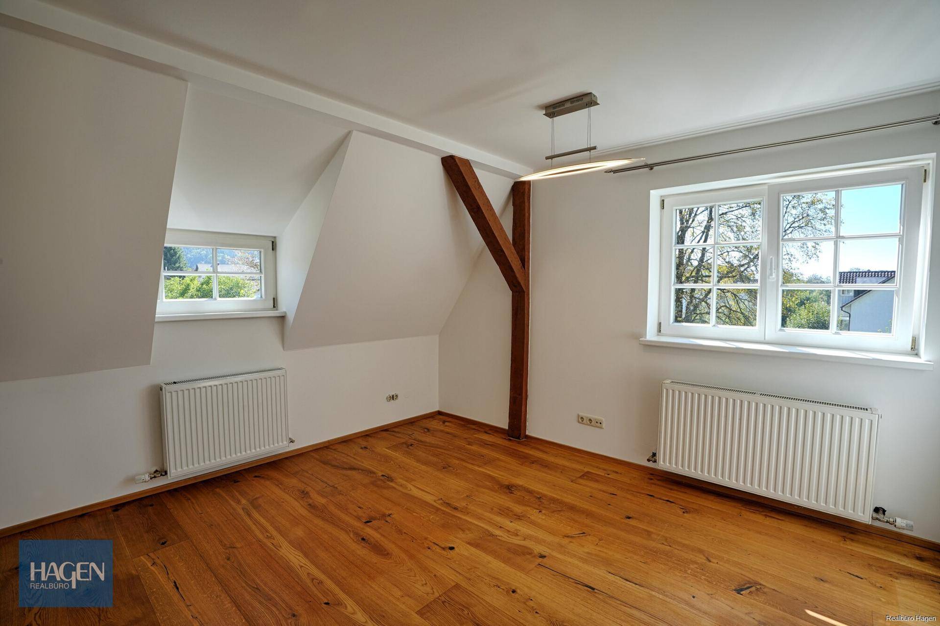 Geräumiges Schlafzimmer im Dachgeschoss mit Holzboden, sichtbarem Holzbalken und Heizkörpern.