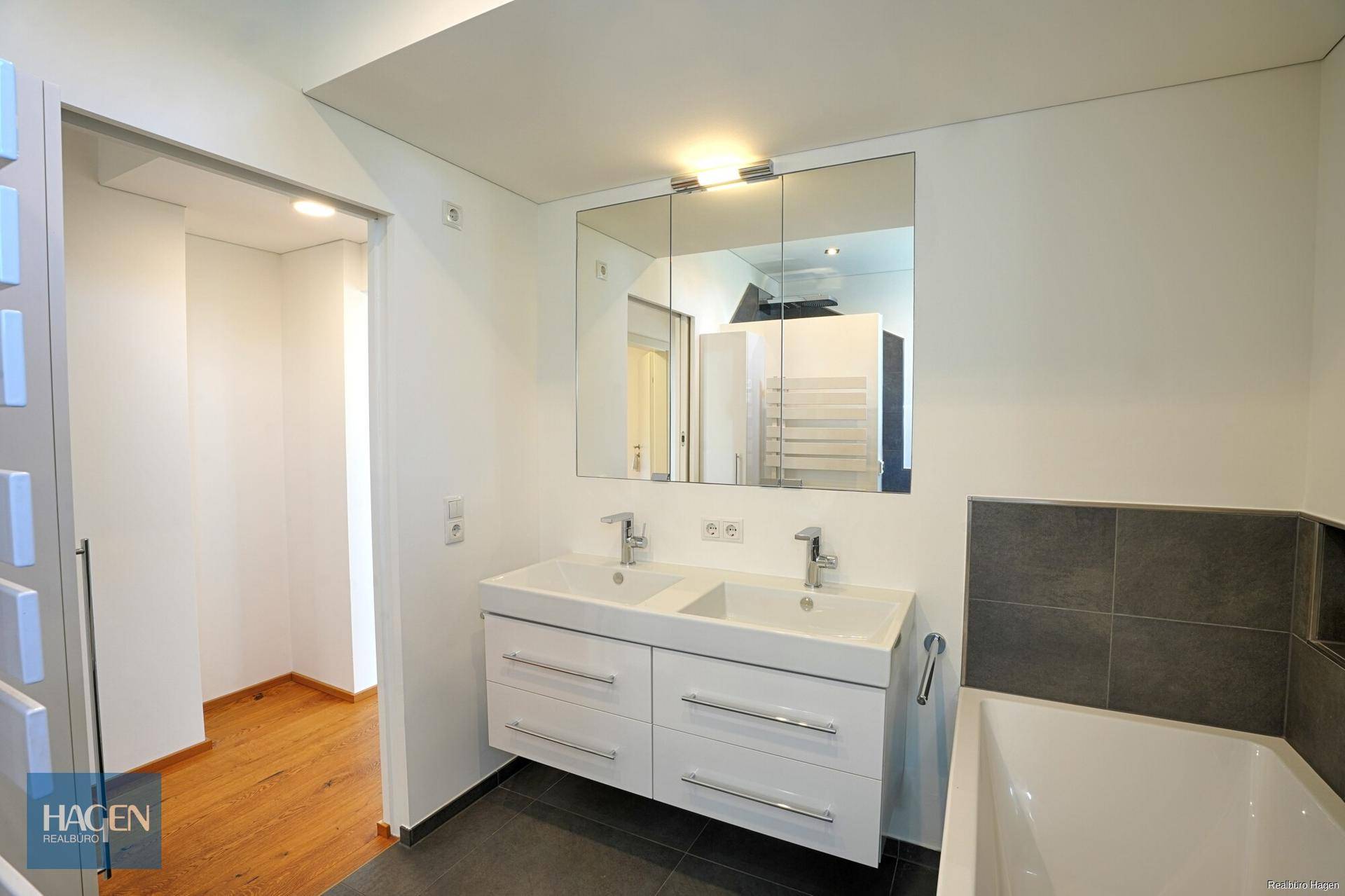 Elegantes Badezimmer mit Doppelwaschbecken, Spiegelschrank und Zugang zu einem weiteren Raum.