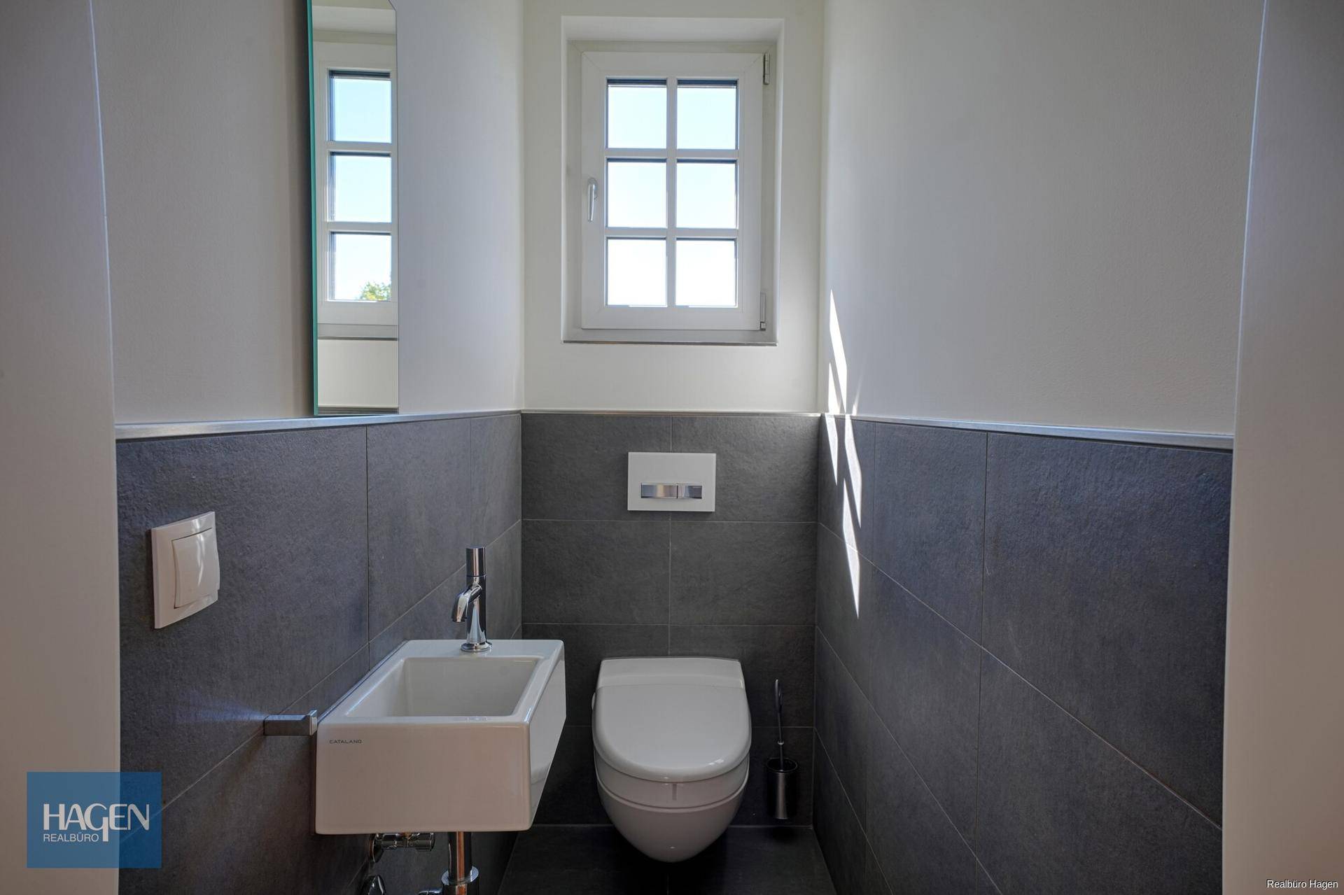 Modernes Gäste-WC mit Wand-WC, kleinem Waschbecken und Fenster für Tageslicht.
