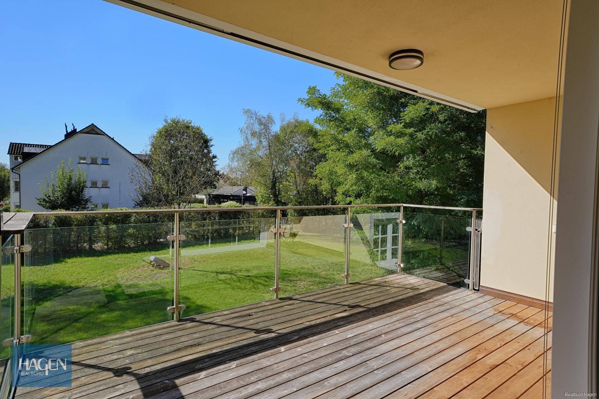 Heller Balkon mit Holzboden und modernem Glasgeländer, ideal für entspannte Stunden im Freien.