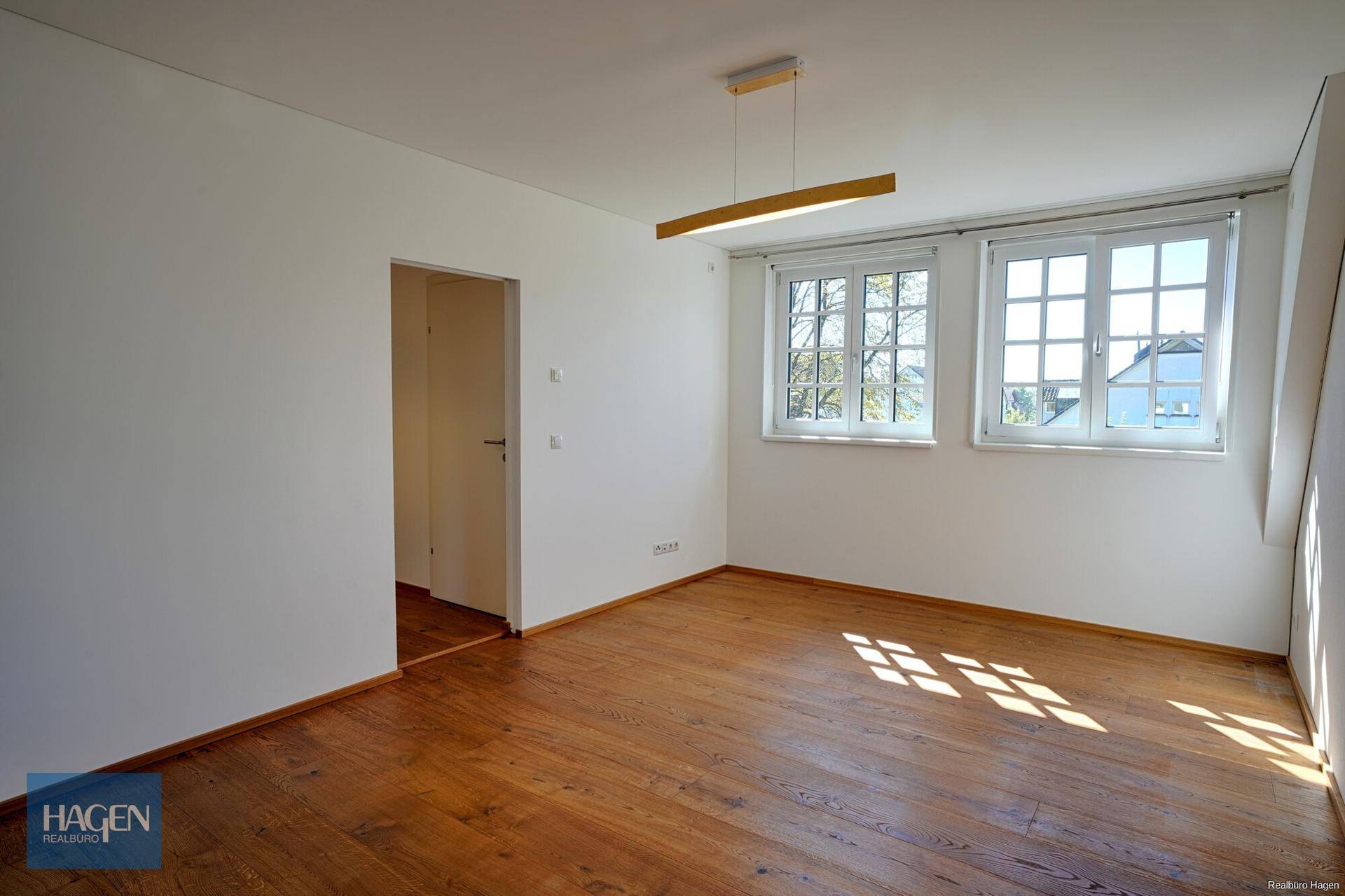Helles Schlafzimmer mit Holzboden und zwei Fenstern, die viel Tageslicht hereinlassen.