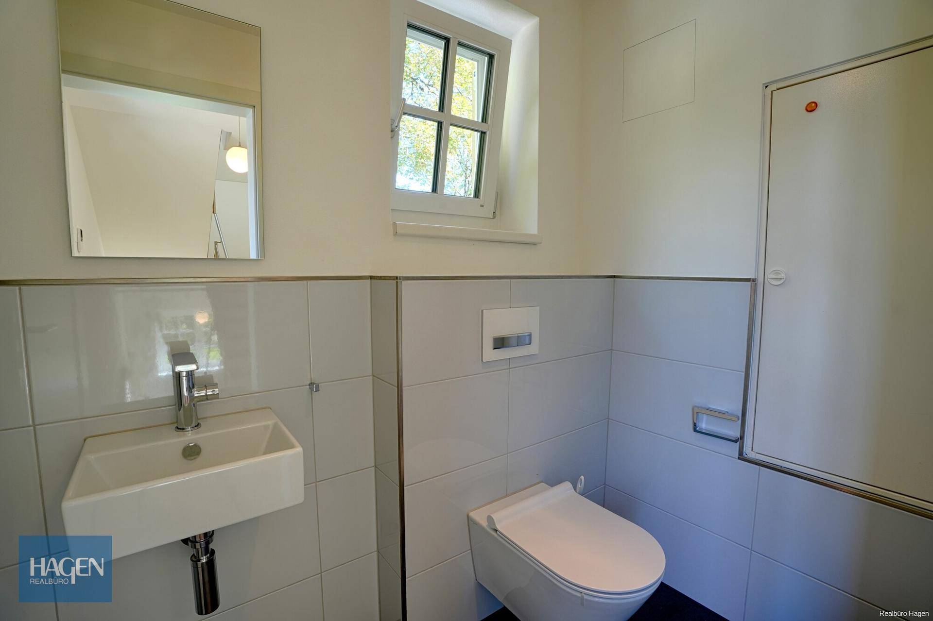 Helles Gäste-WC mit modernen Fliesen, Wand-WC und einem Fenster für natürliche Belüftung.