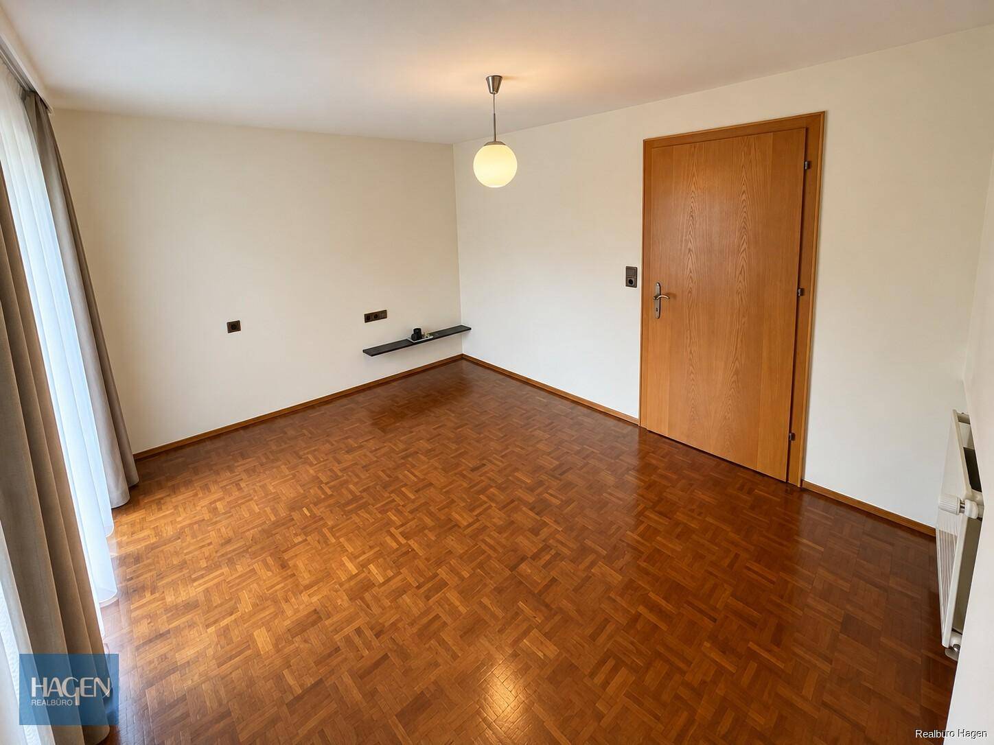 Helles Schlafzimmer mit Parkettboden und großem Fenster, unmöbliert.