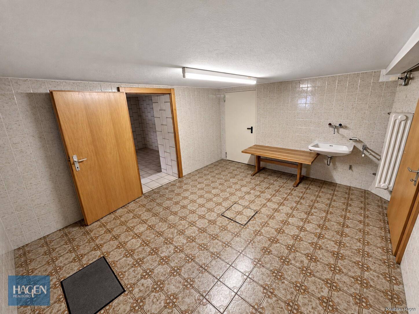 Großer Kellerraum mit Fliesenboden, Waschbecken und Zugang zu weiteren Räumen.