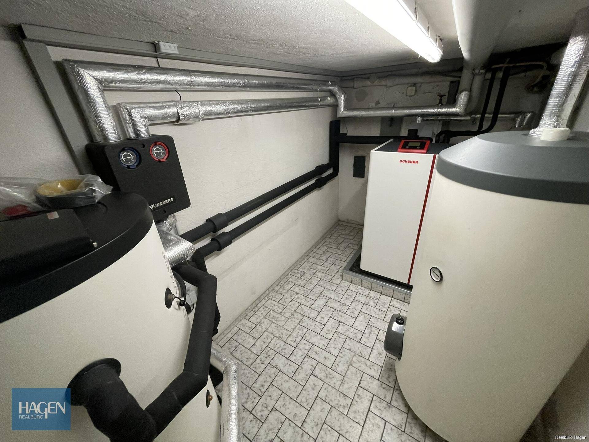 Heizungsraum im Keller mit modernen Heizungsanlagen und isolierten Rohren für effiziente Wärmeversorgung.