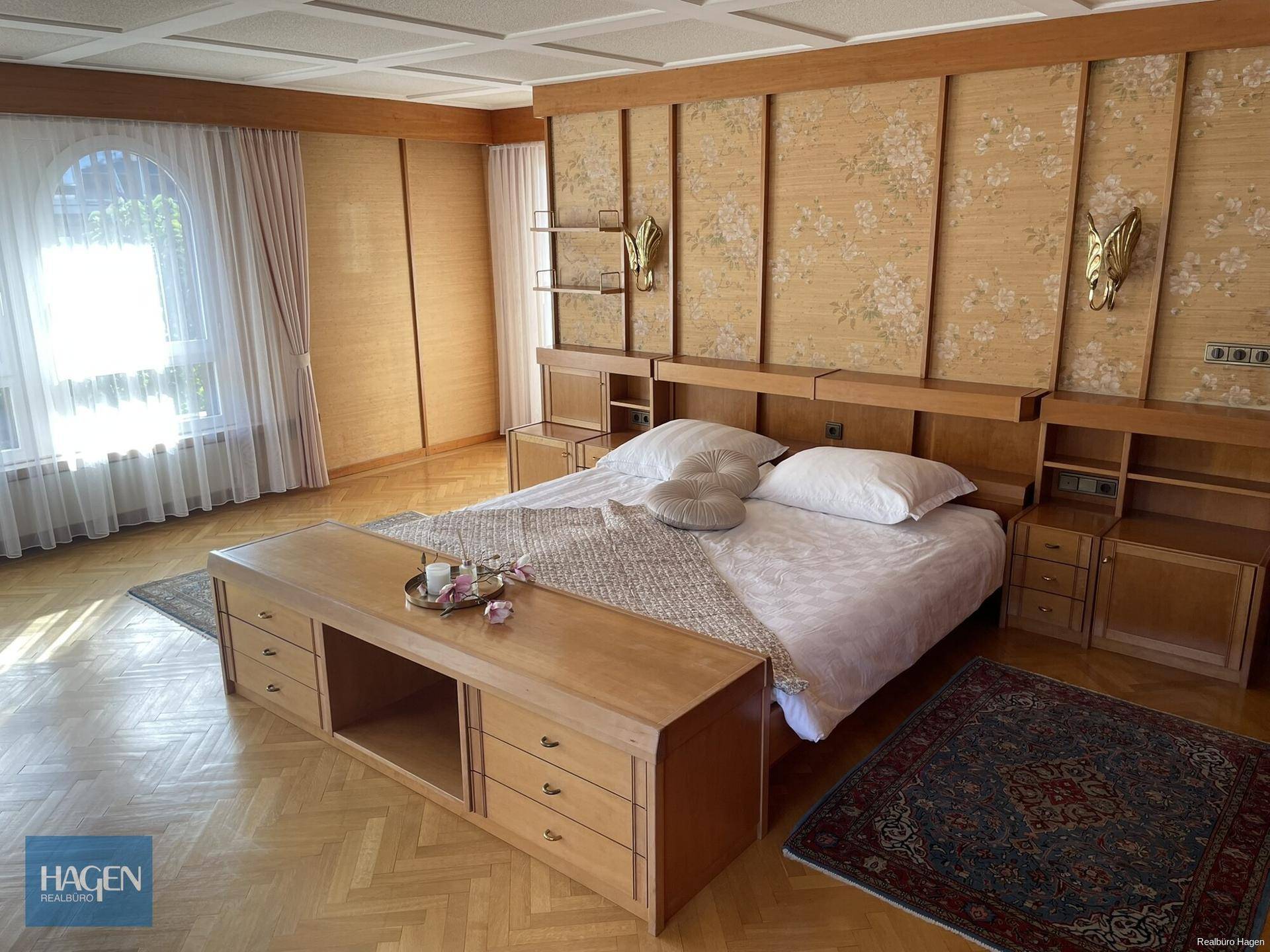 Elegantes Schlafzimmer mit Doppelbett, Parkettboden und floraler Wandgestaltung.
