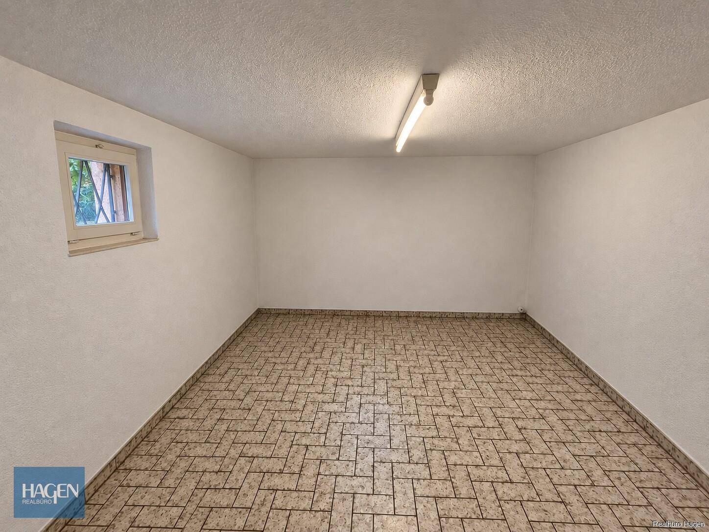 Heller Kellerraum mit Fliesenboden und kleinem Fenster.
