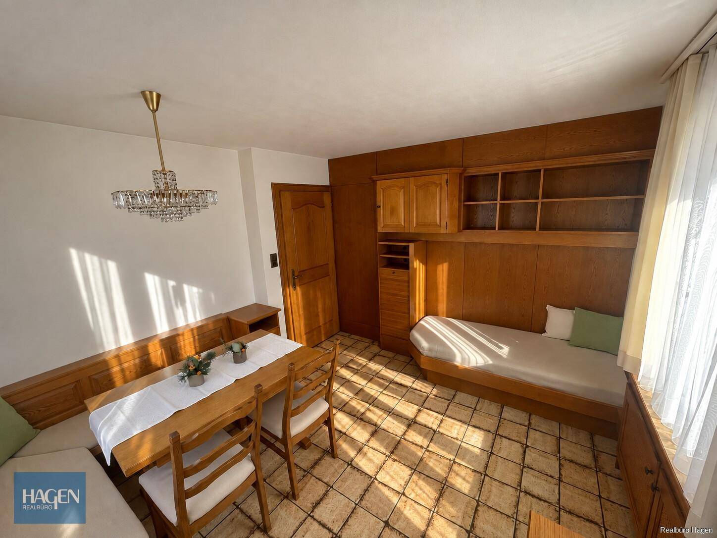 Helles Zimmer mit Einzelbett, Esstisch und Holzvertäfelung.